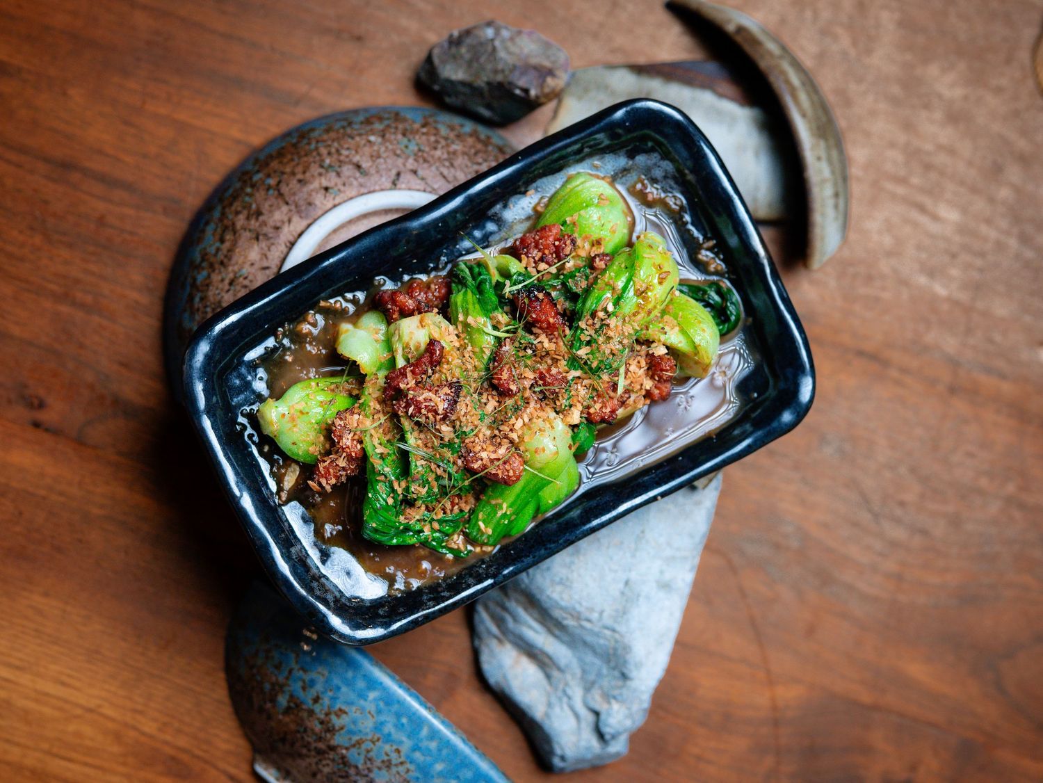 Spicy stir-fried bok choy with chili flakes and sesame seeds served in a black rectangular dish on a wooden table.
