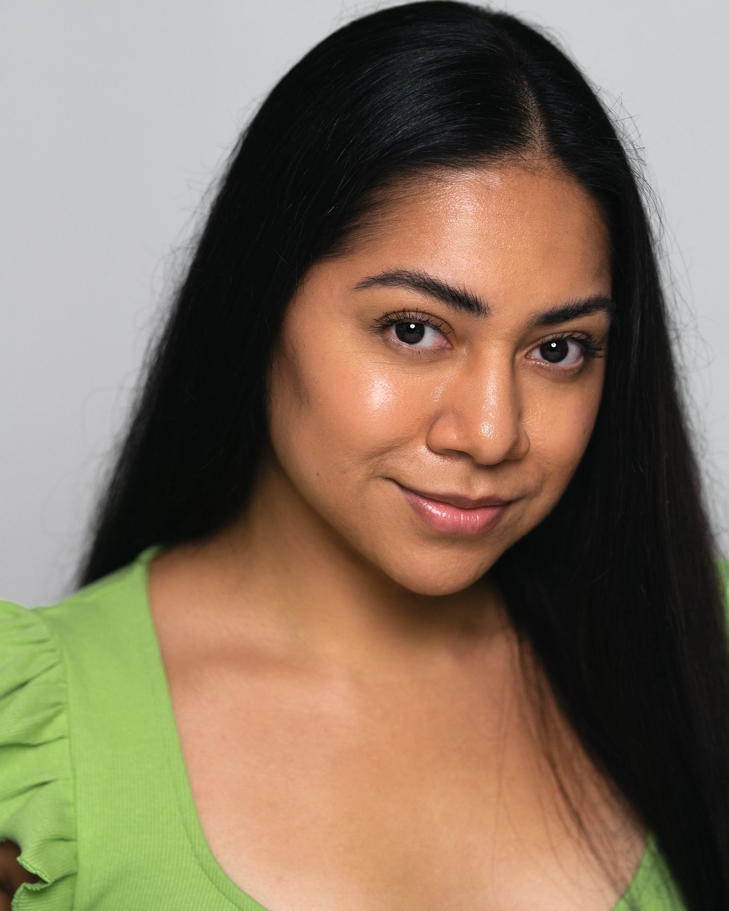 Young woman with long black hair wearing a green top, smiling softly against a light gray background.