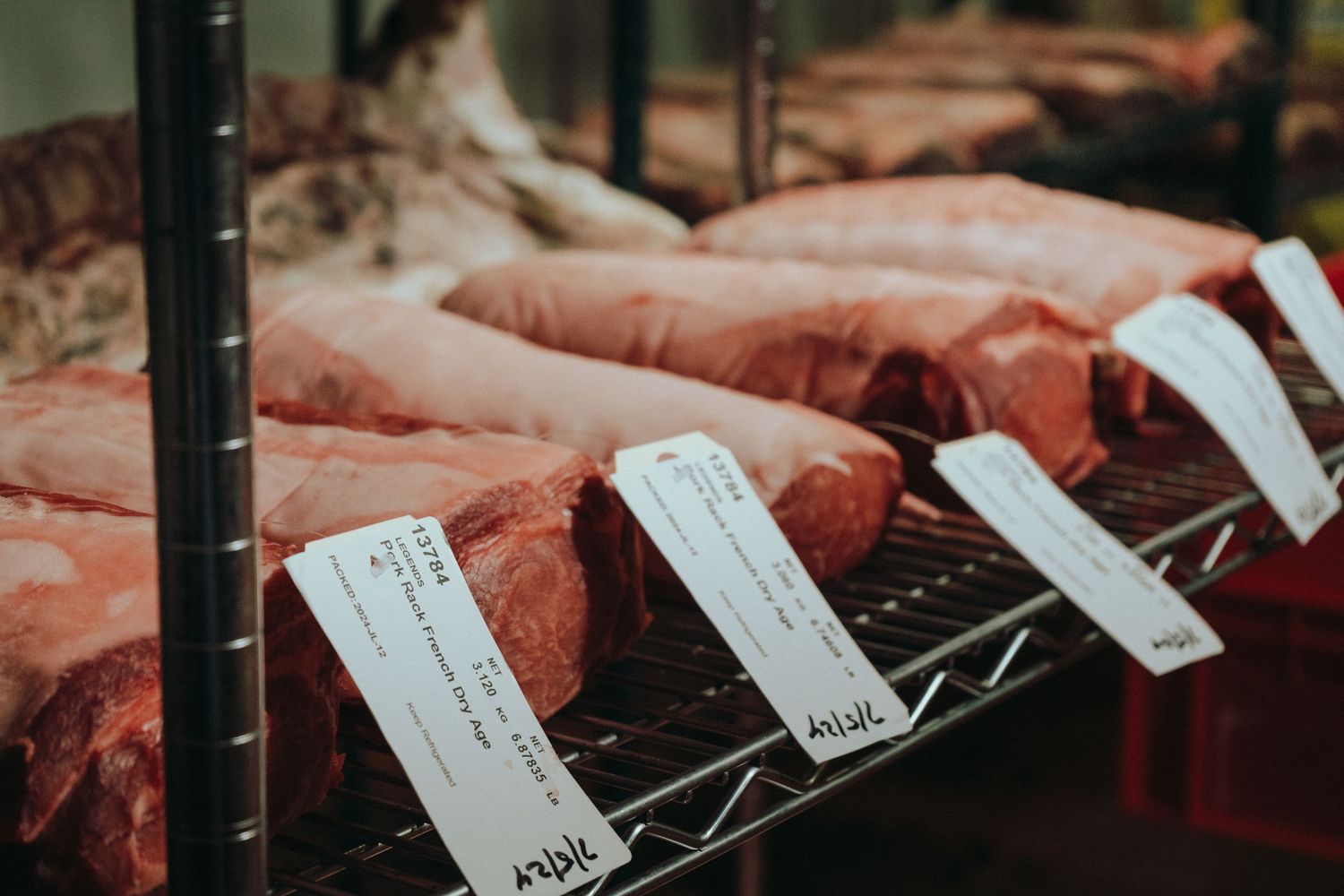 Fresh cuts of raw beef displayed on a metal rack with price tags at a butcher shop.