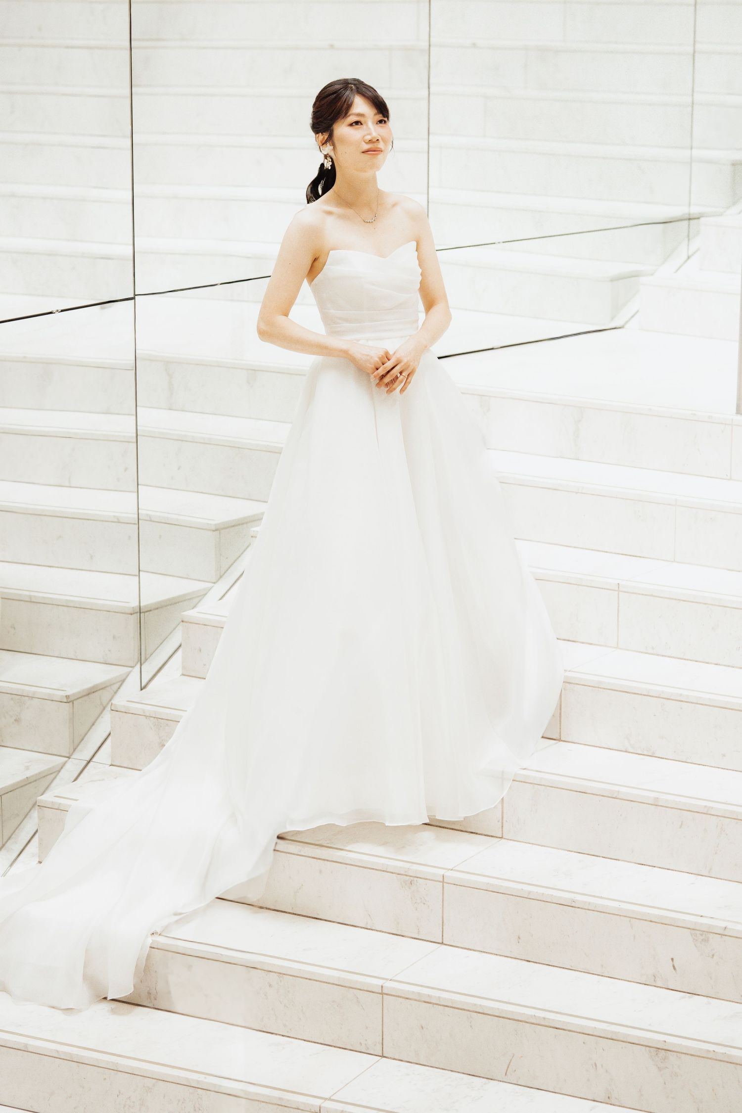 Elegant bride in a white ball gown with sheer bodice standing gracefully on marble stairs.