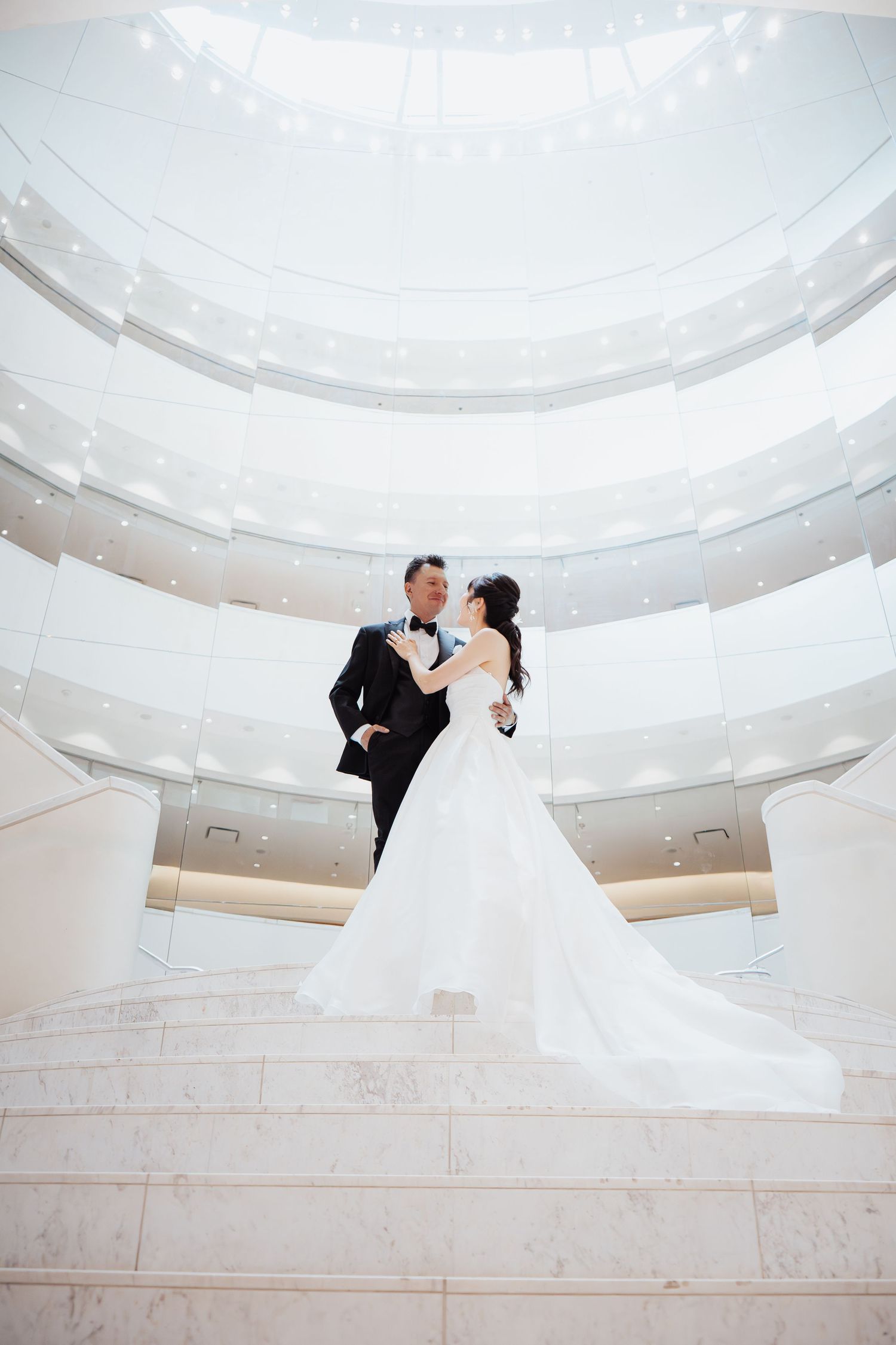 Bride and groom embrace on marble stairs beneath a stunning domed ceiling in an elegant wedding venue.