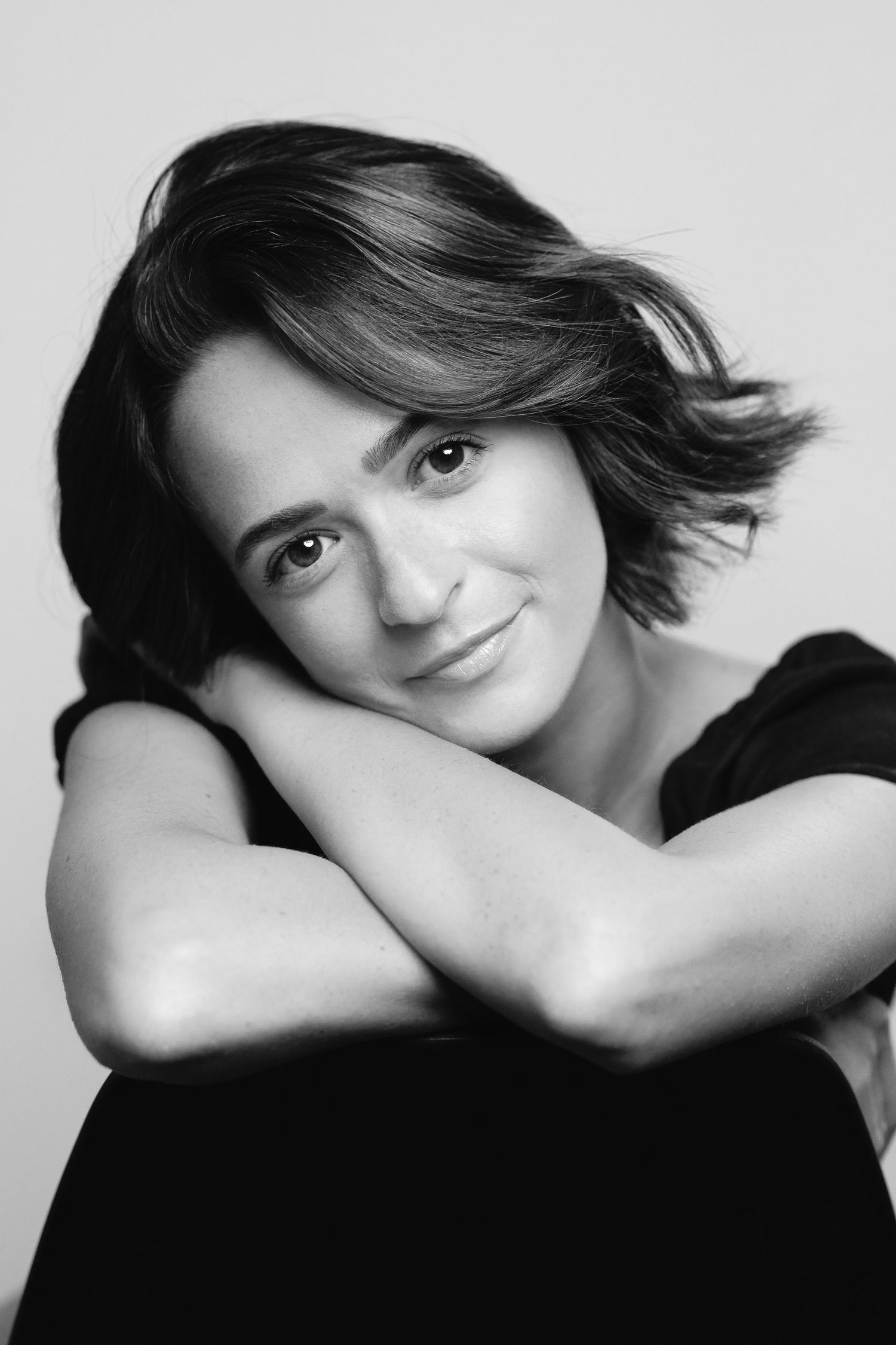 Black and white portrait of a young woman with short hair, arms crossed, smiling softly at camera.