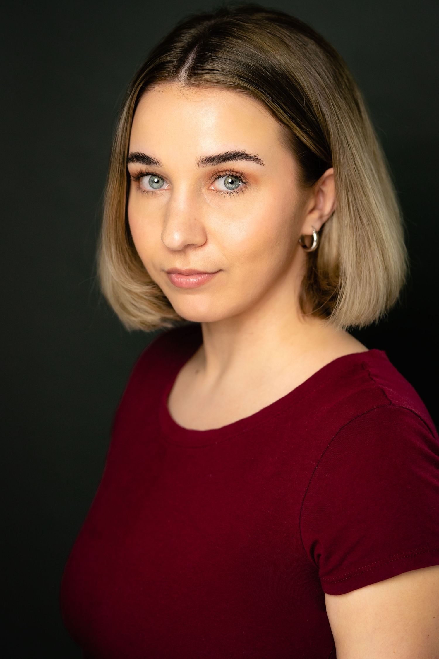 Young woman with blonde bob hair and blue eyes wearing a red top, posing for a professional headshot photo.
