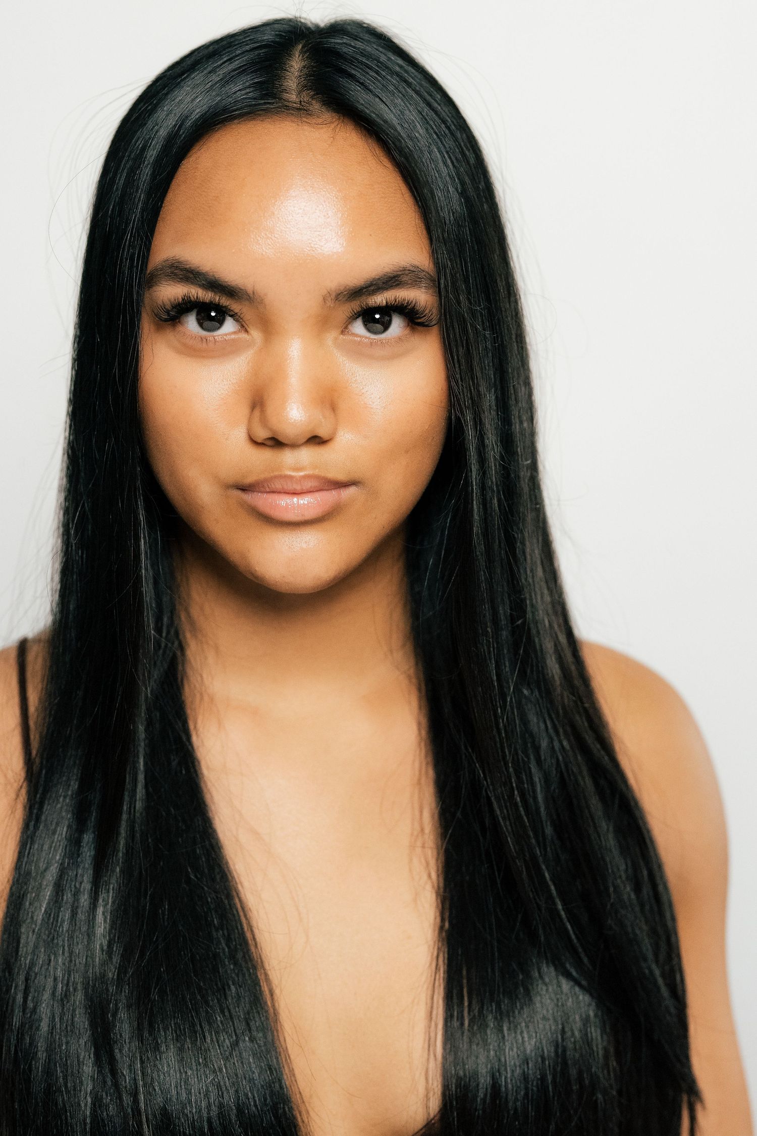 Young woman with long straight black hair posing against a light gray background in a portrait shot.