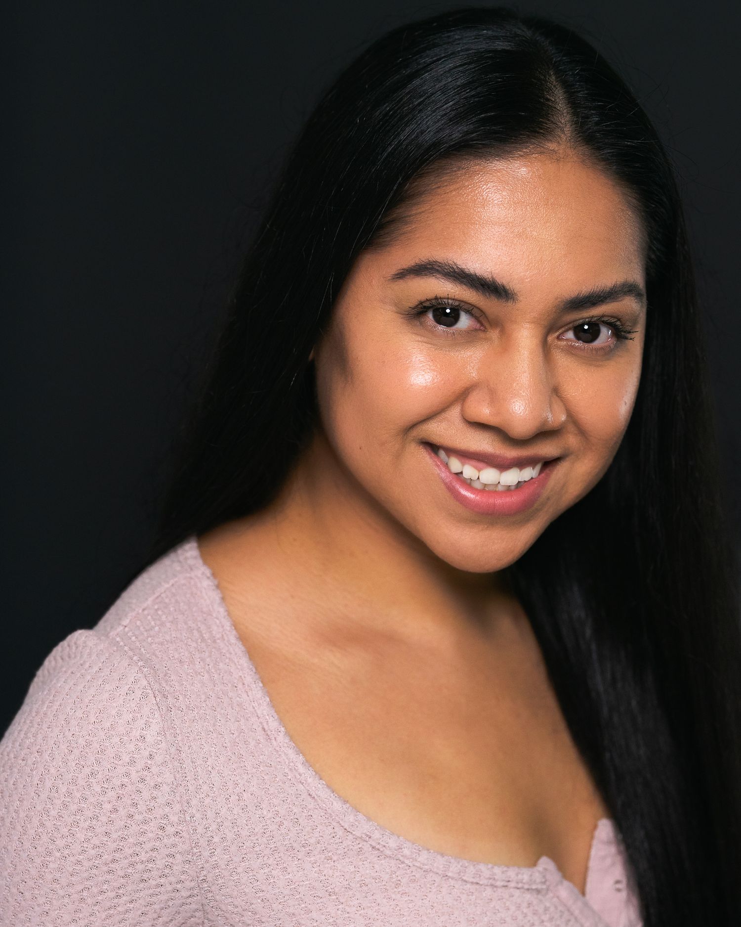 A young woman with long dark hair smiles warmly in a professional headshot against a dark background.