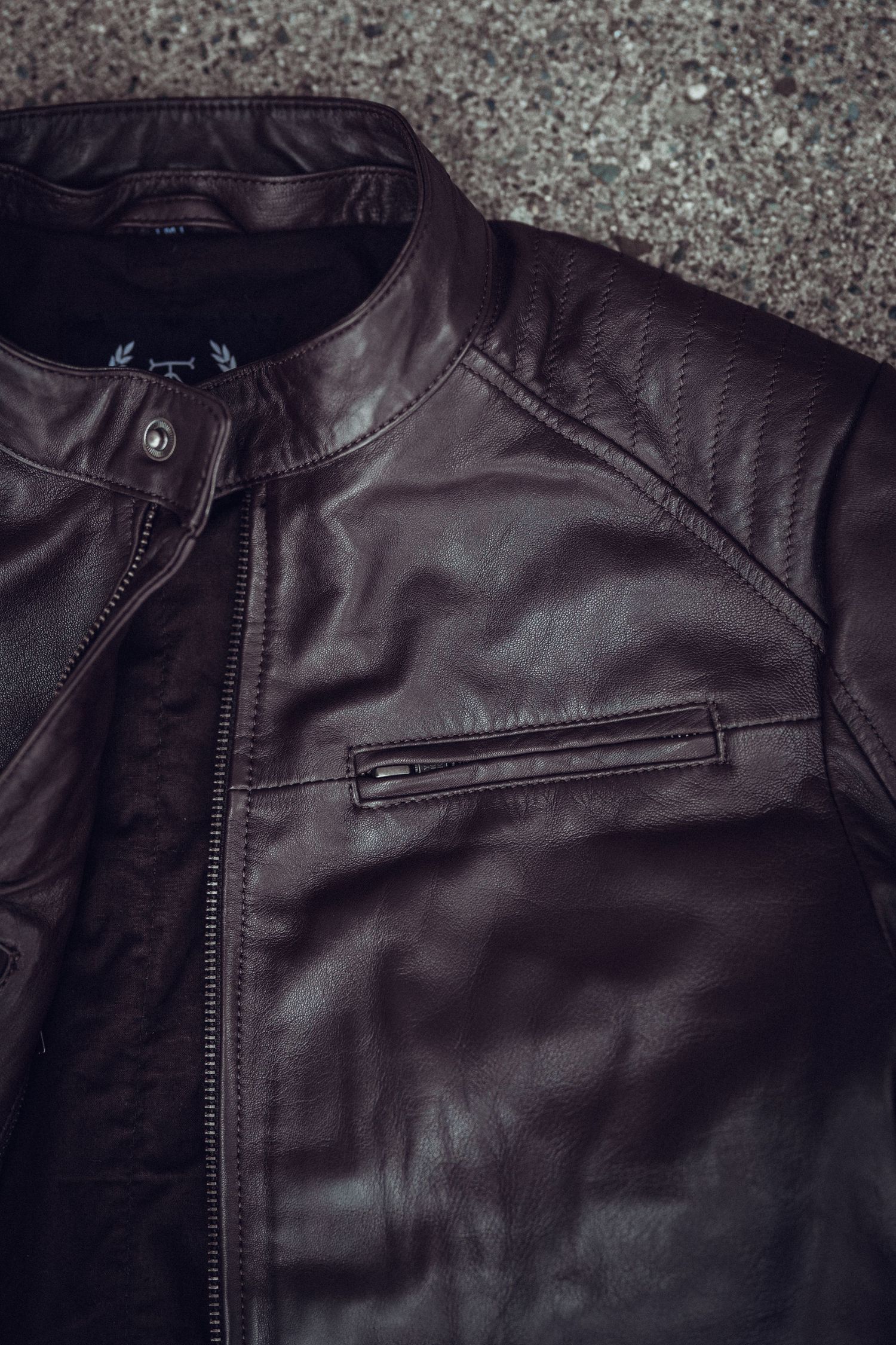 Dark brown leather motorcycle jacket with zipper details and quilted shoulders, laid flat on gray surface.