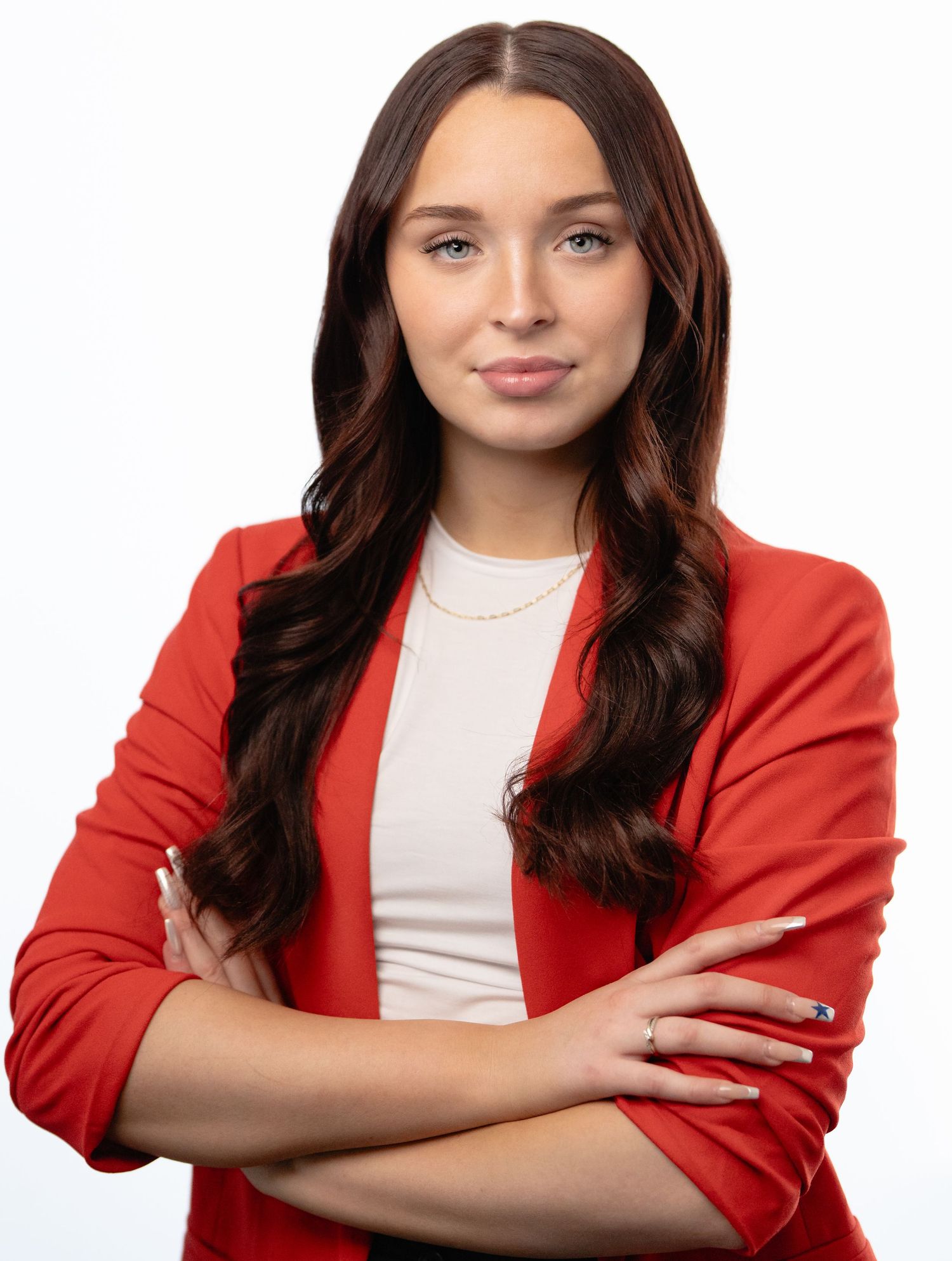 Professional woman in red blazer with arms crossed, long dark hair, smiling confidently against white background. Professional Headshots Van