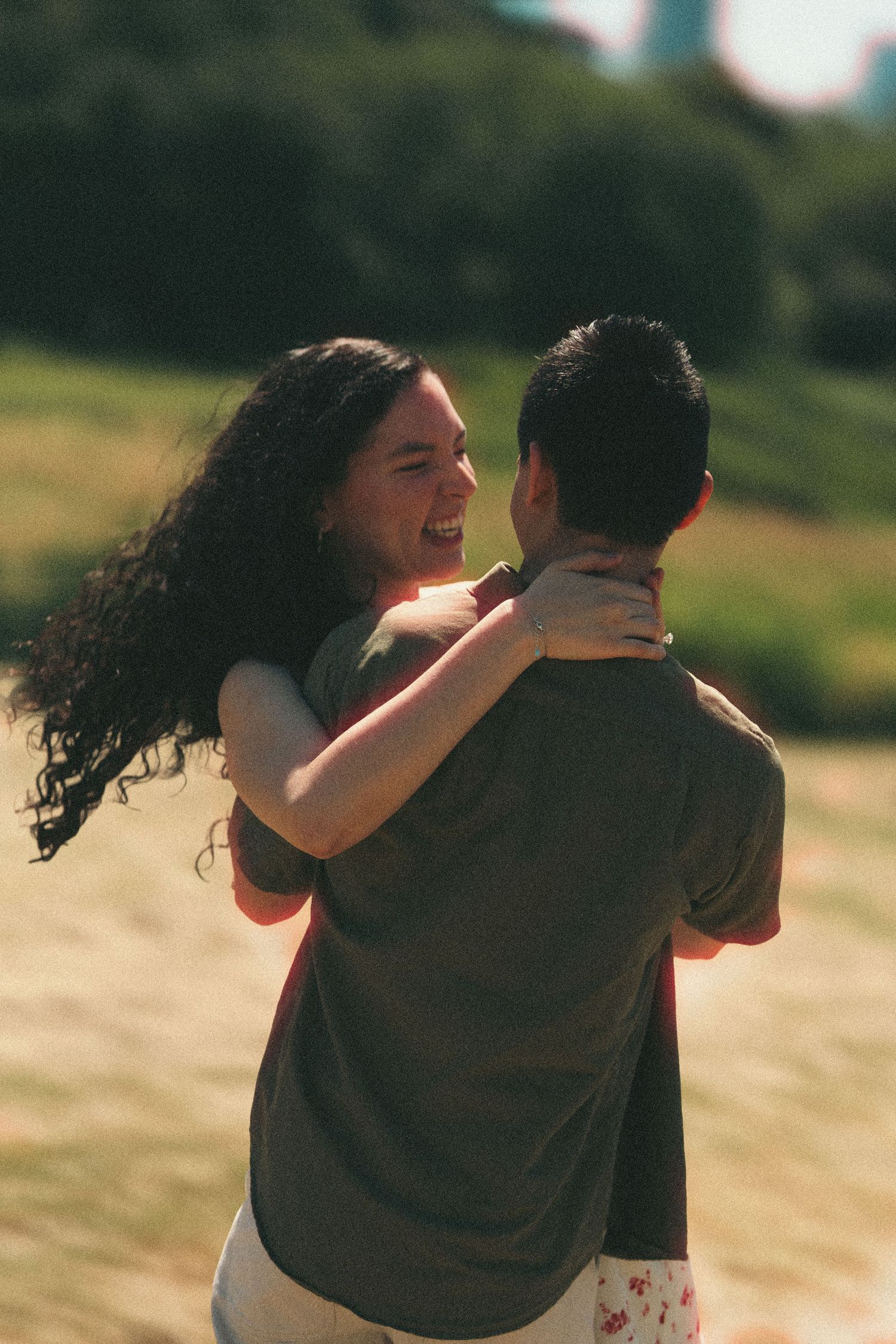 A joyful couple dances and laughs together outdoors in warm sunset light, the woman's curly hair flowing.