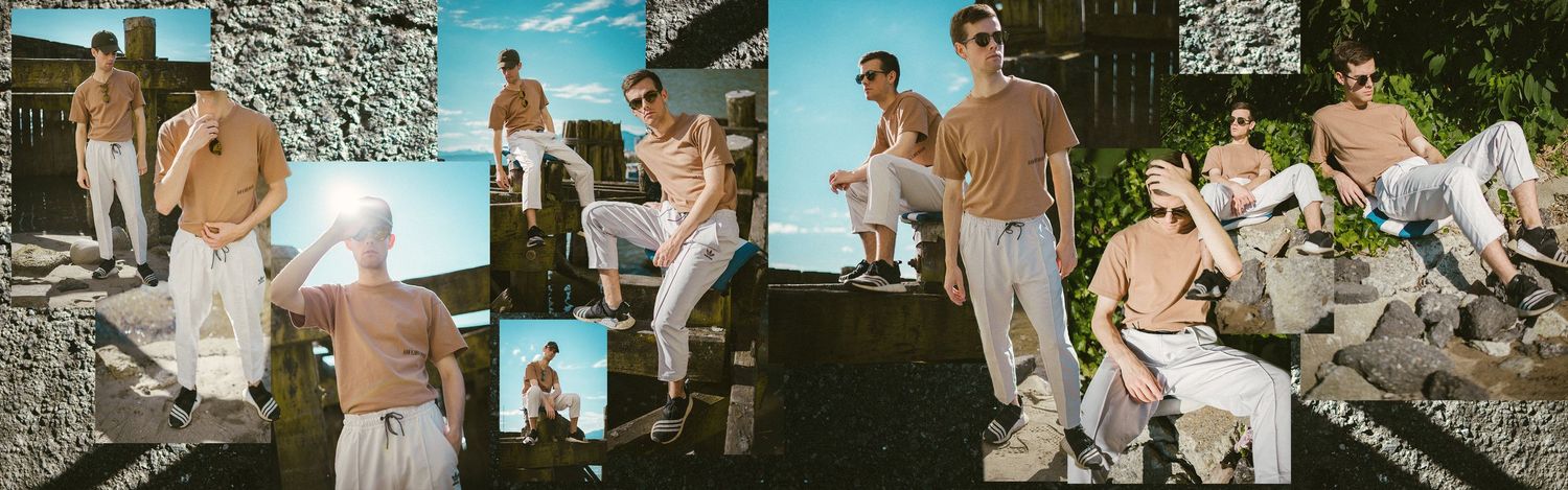 Two men pose outdoors in casual beige and white outfits against a stone wall backdrop in a stylish fashion editorial. Lifestyle/product