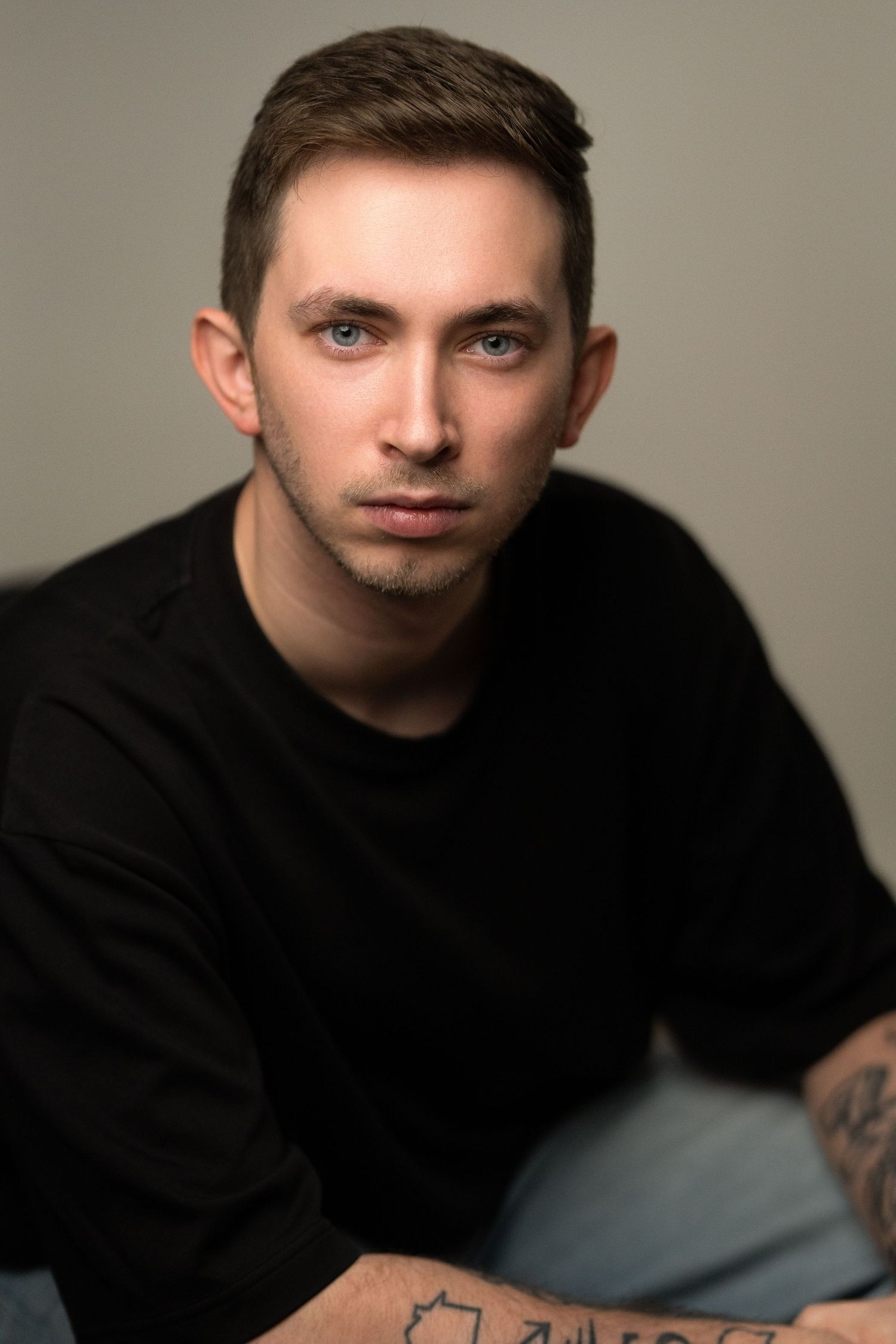 Young man with blue eyes and tattoos wearing a black sweater, posed for a professional portrait photo.
