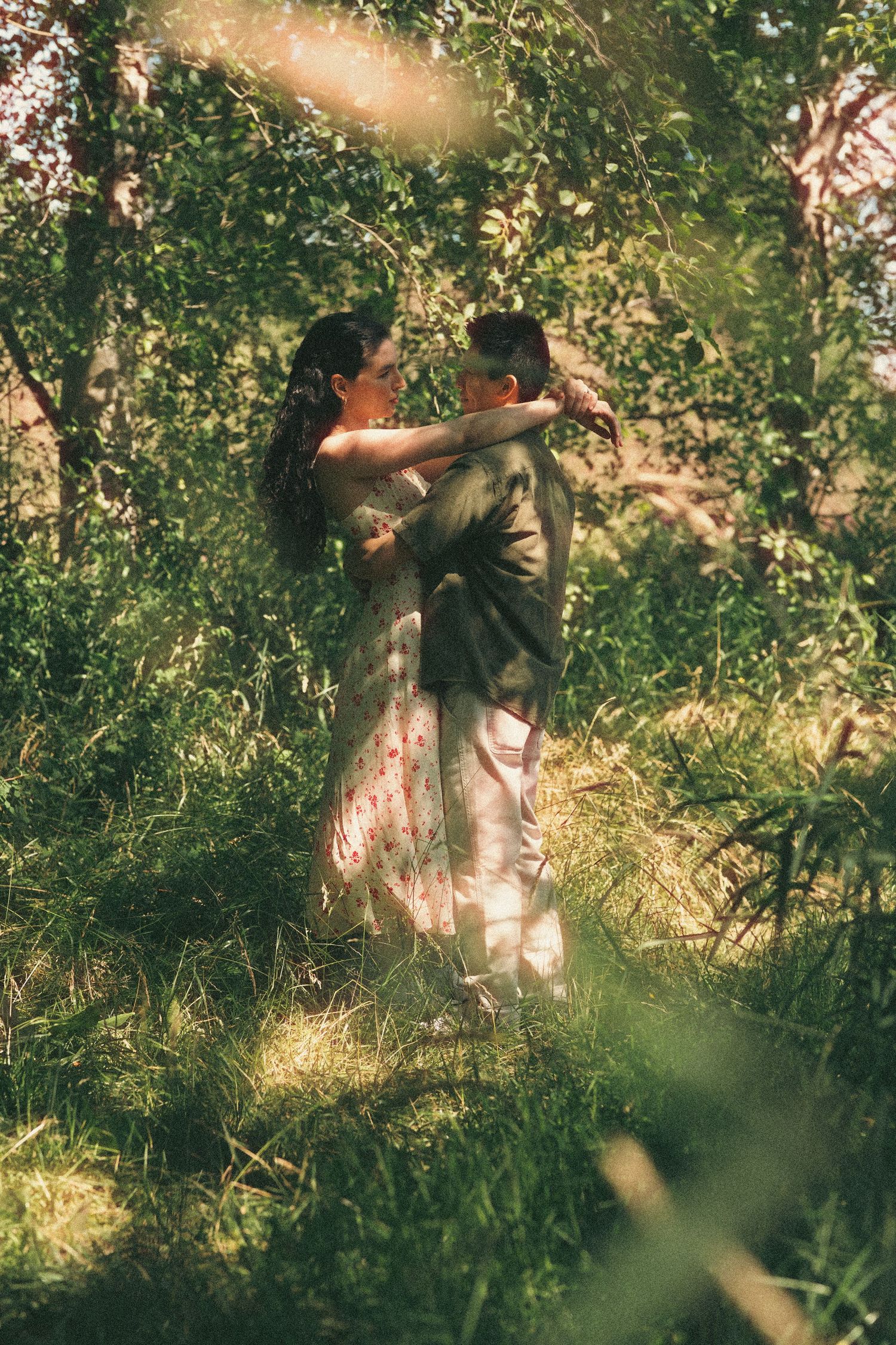 Couple dancing romantically in a lush green forest, woman in floral dress embracing man in suit.