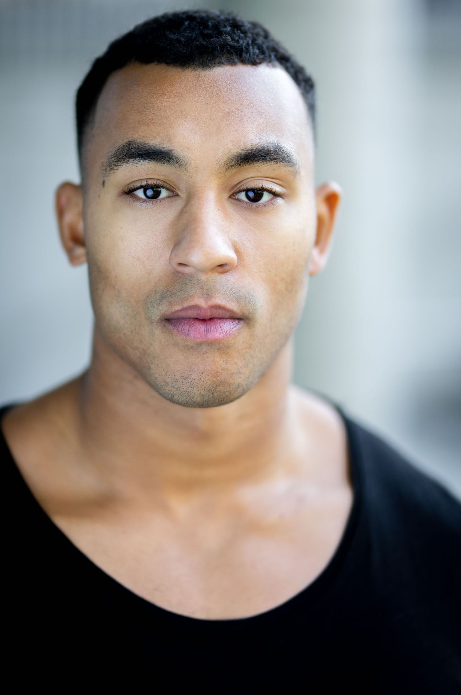 Young man in black scoop-neck shirt with short hair poses for a professional headshot portrait.