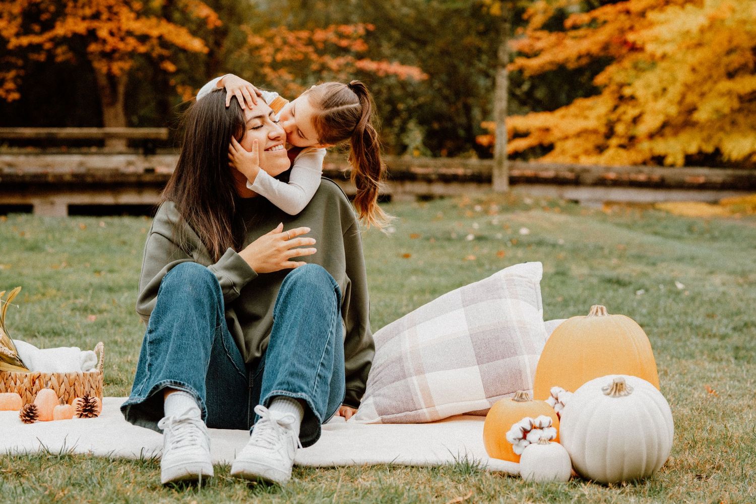 Mother and child share a tender moment on a blanket during a fall outdoor picnic with pumpkins and autumn foliage.