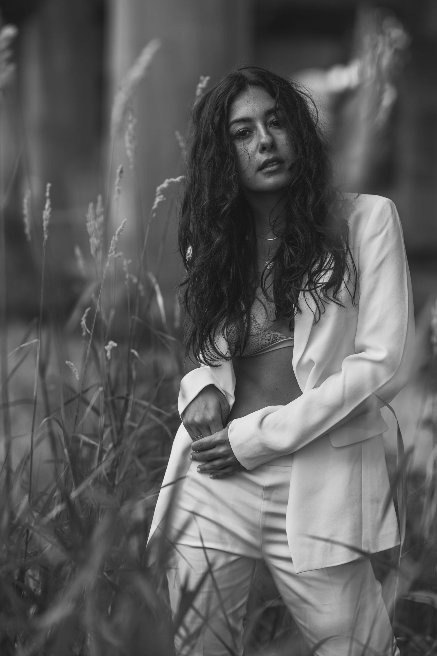 Black and white portrait of a woman in a white suit standing among tall grass in an outdoor setting.Lifestyle photography vancouver