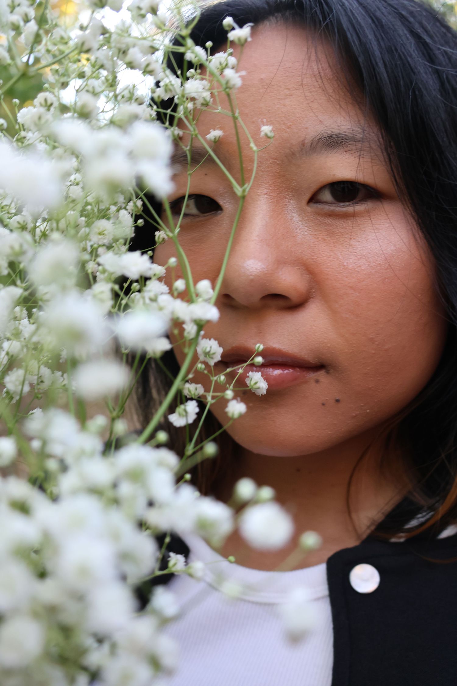 Close-up portraits of a person with small white flowers against a soft natural background.