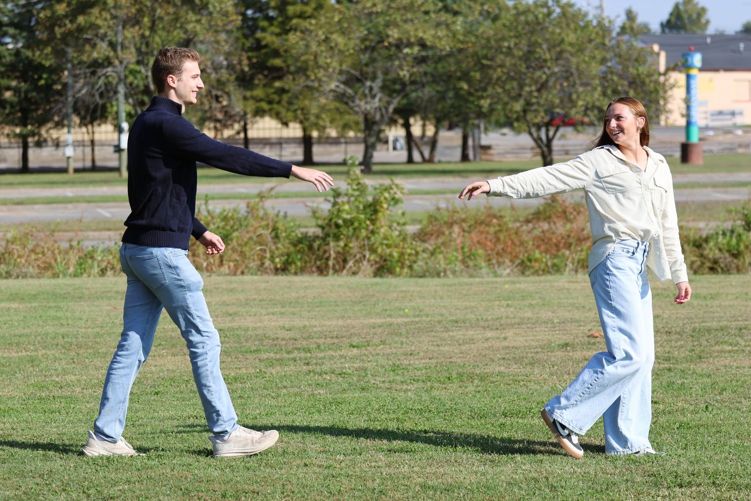 Two people practice dance moves together on a sunny lawn.
