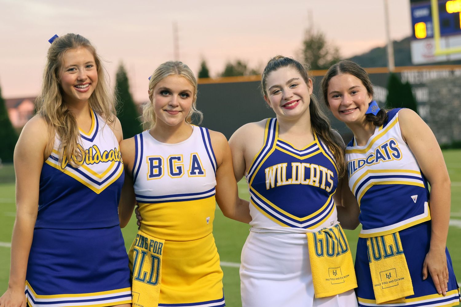 Cheerleaders in blue, yellow and white uniforms pose together at a sports event.