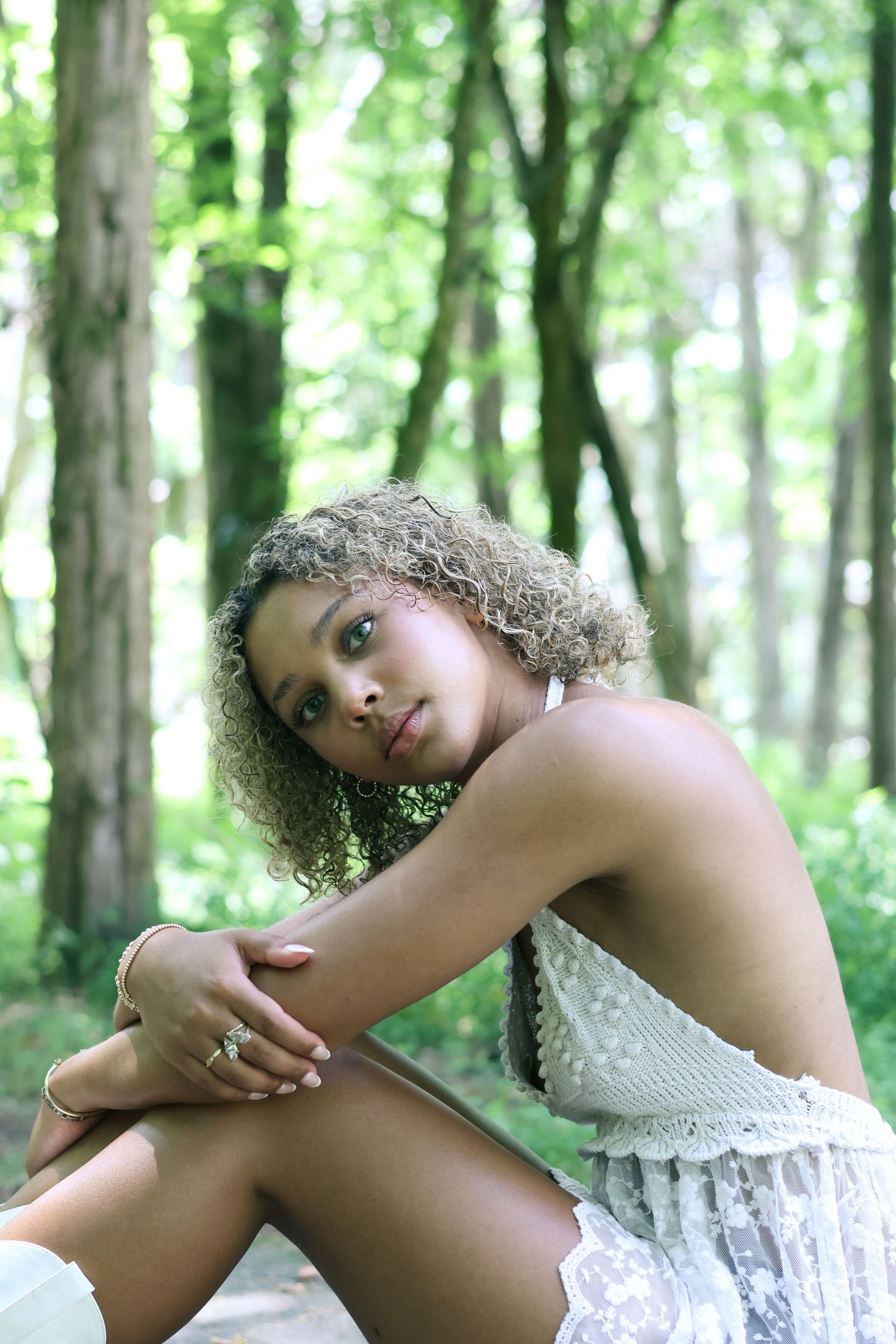 Artistic outdoor portrait in white lace dress amid forest scenery.