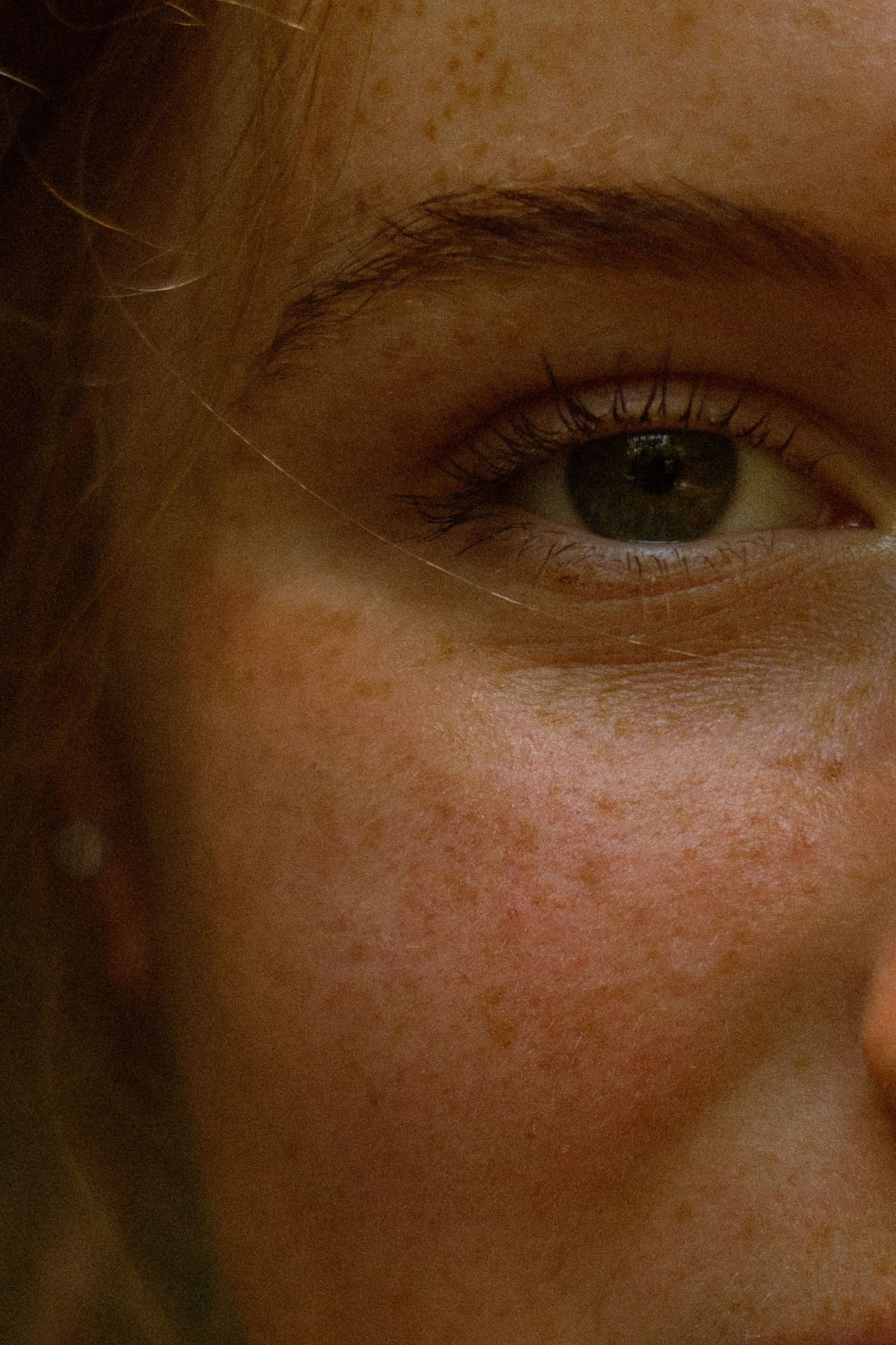 Close-up portrait of a freckled woman with green eyes and blonde hair, showcasing natural skin texture.