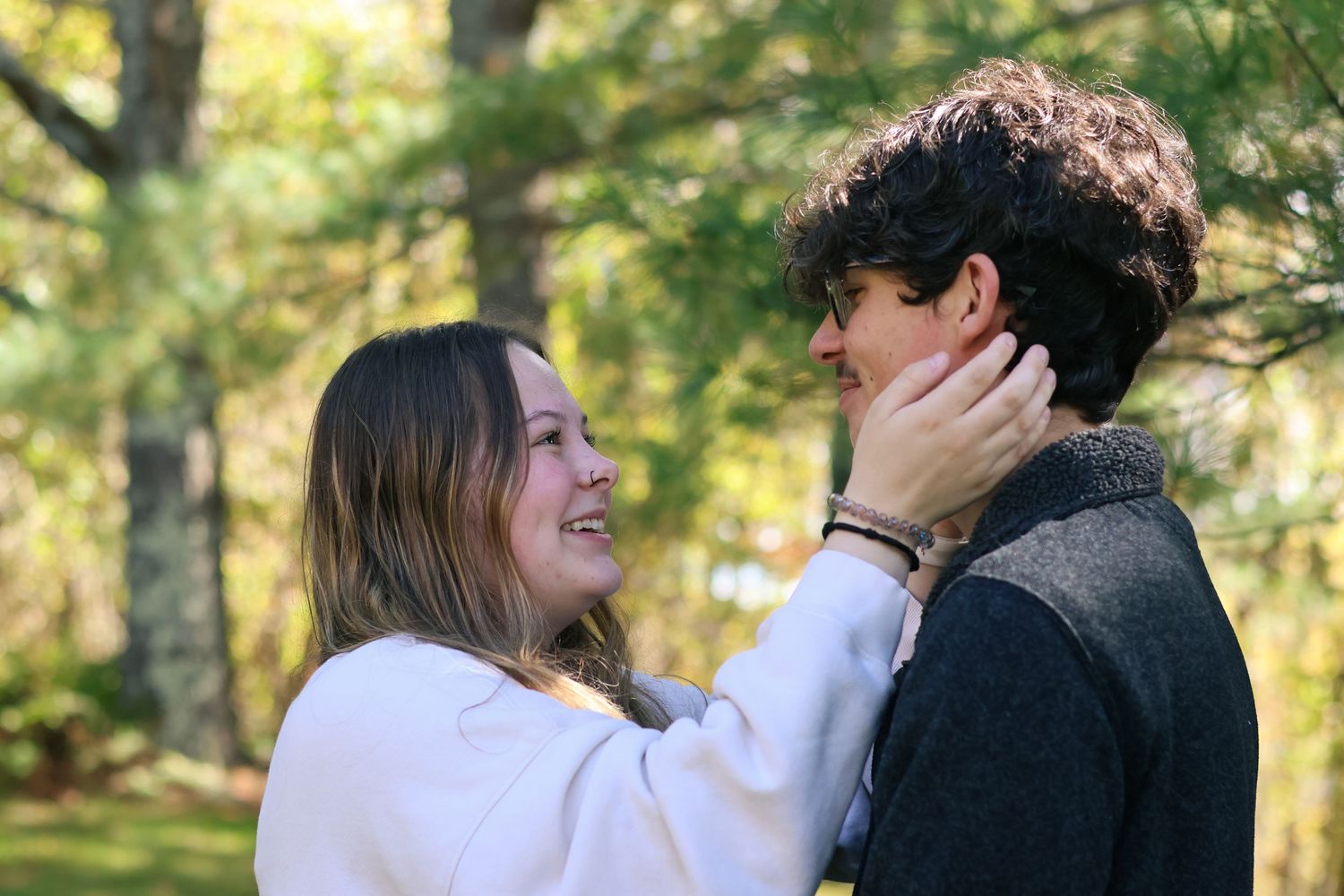 A romantic moment captured between two people in a sunlit forest setting.