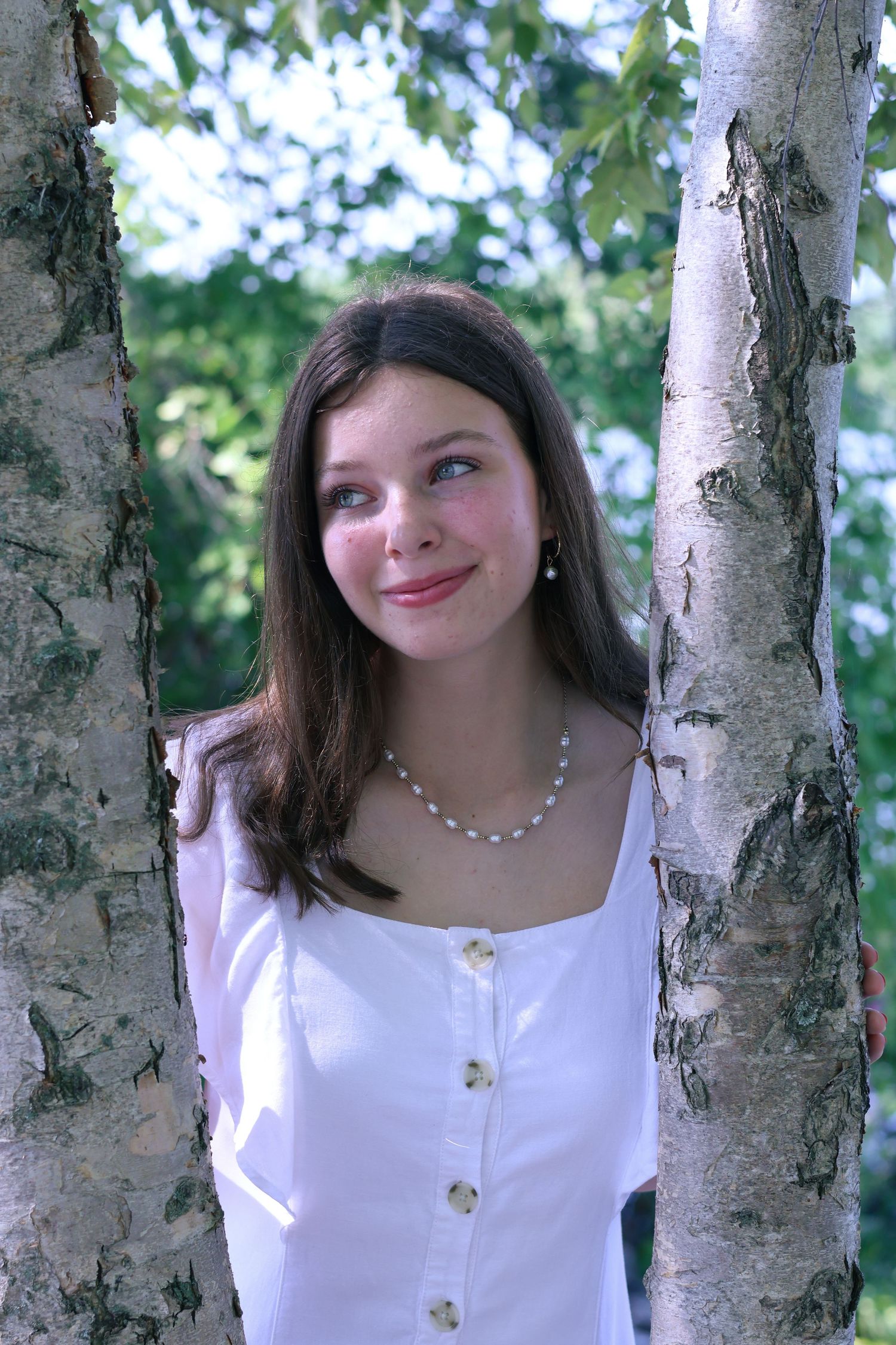 Woman in white square-neck dress poses between white birch tree trunks.