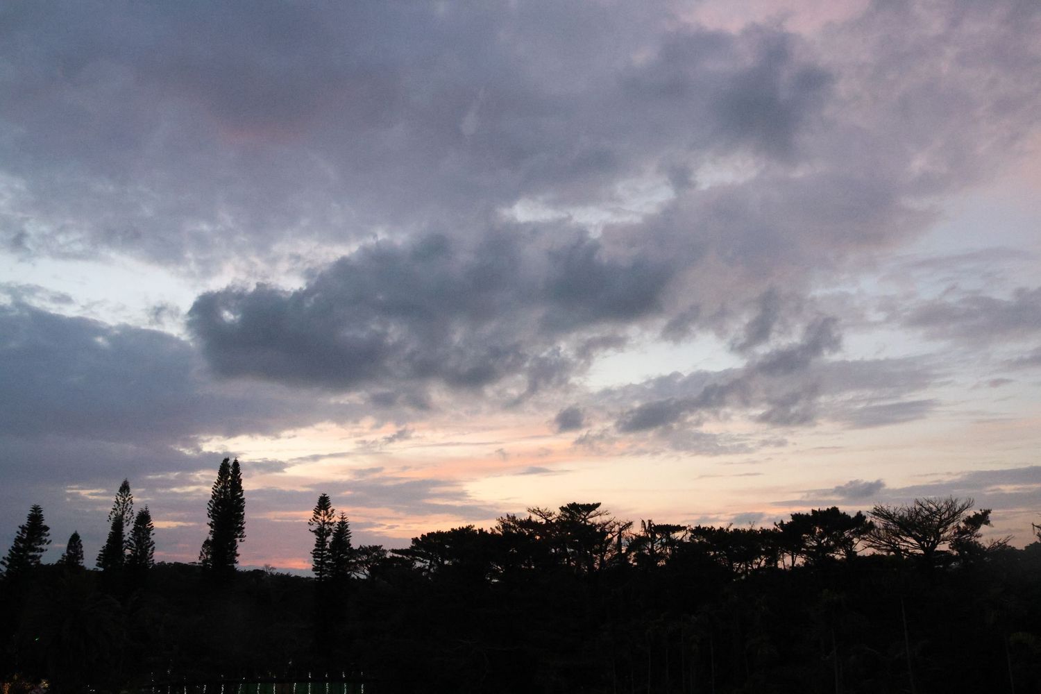 Dramatic sunset sky with dark clouds and silhouetted trees along the horizon.