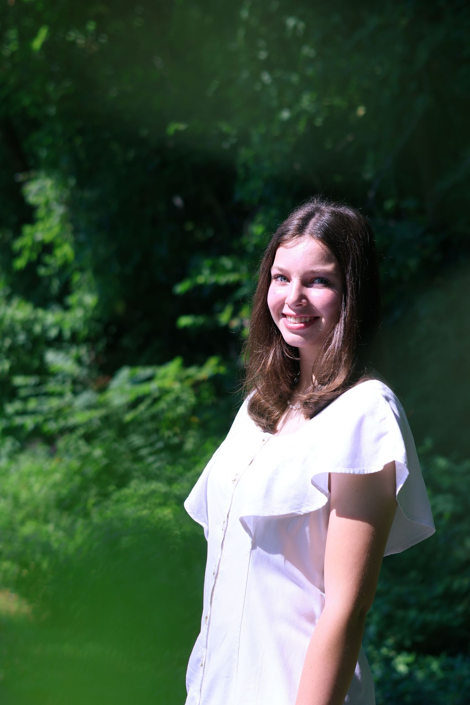 Person in white outfit smiling outdoors against a natural green background.