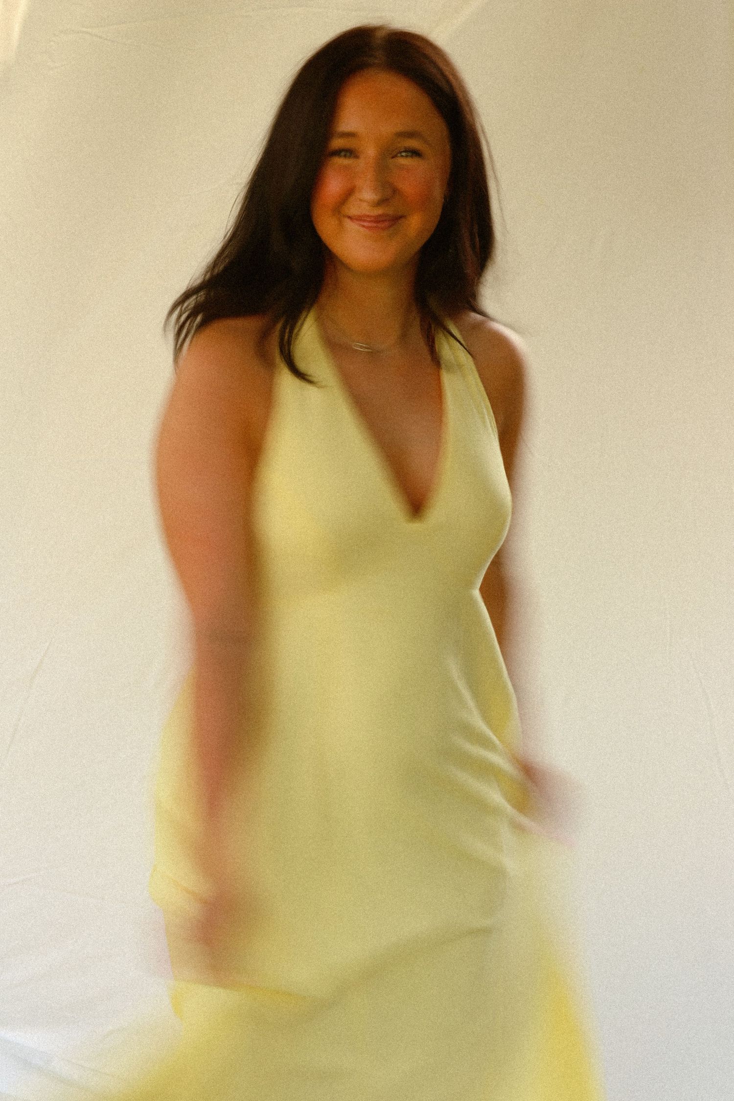 Woman in yellow halter dress spinning gracefully against white backdrop.