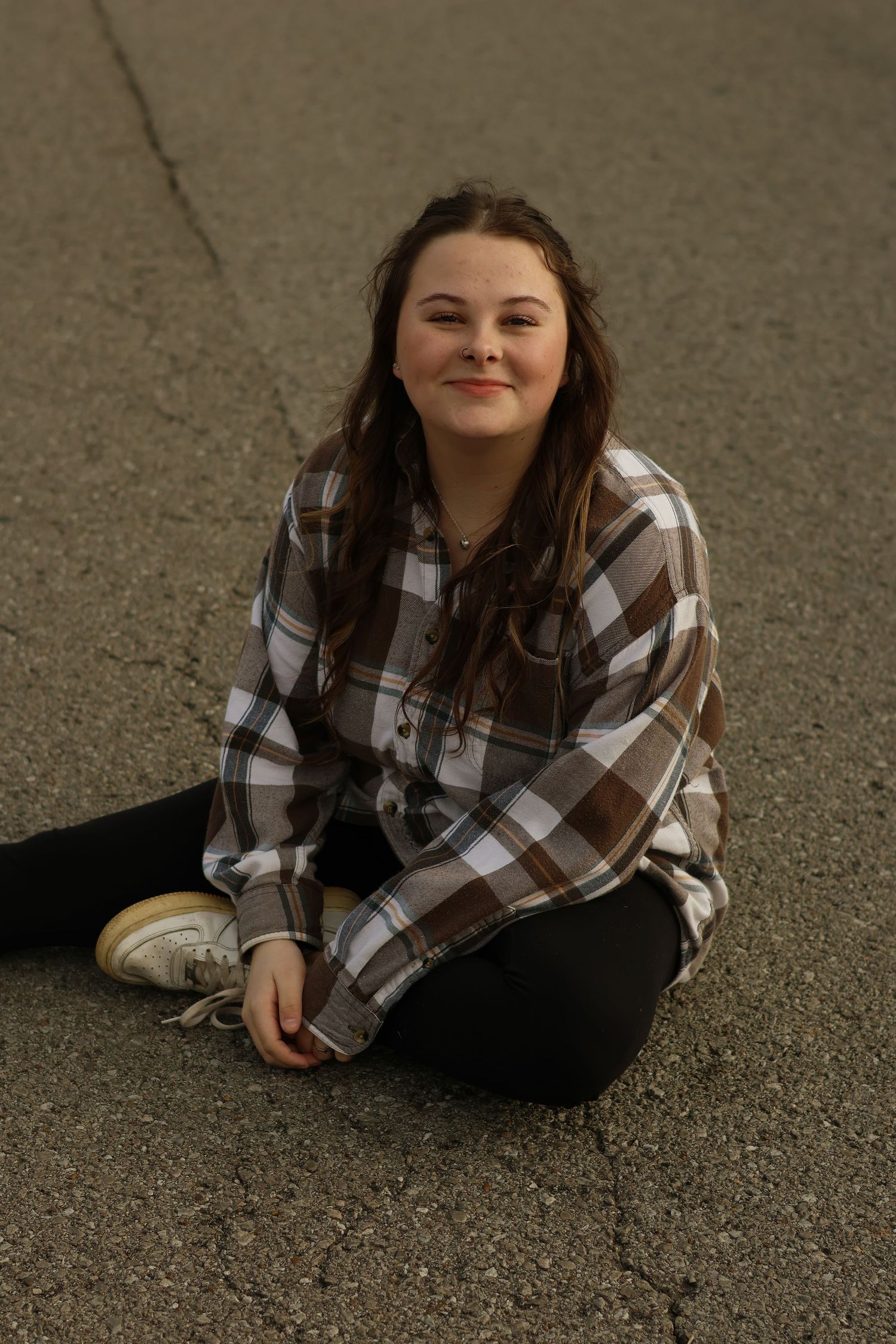 A person in a brown plaid shirt sitting casually on a concrete surface with a relaxed expression.