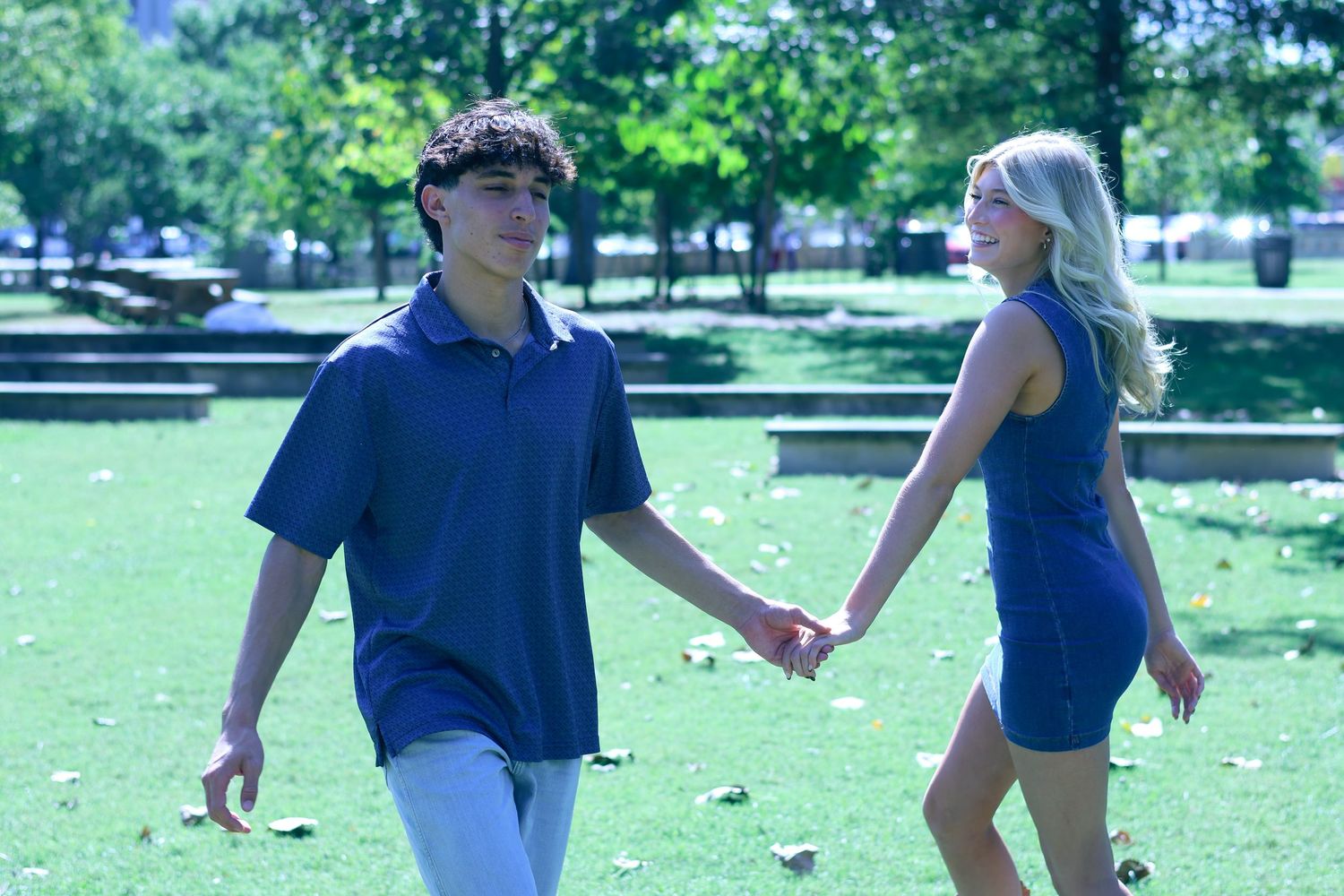 Two people in blue outfits hold hands while walking through a green park.