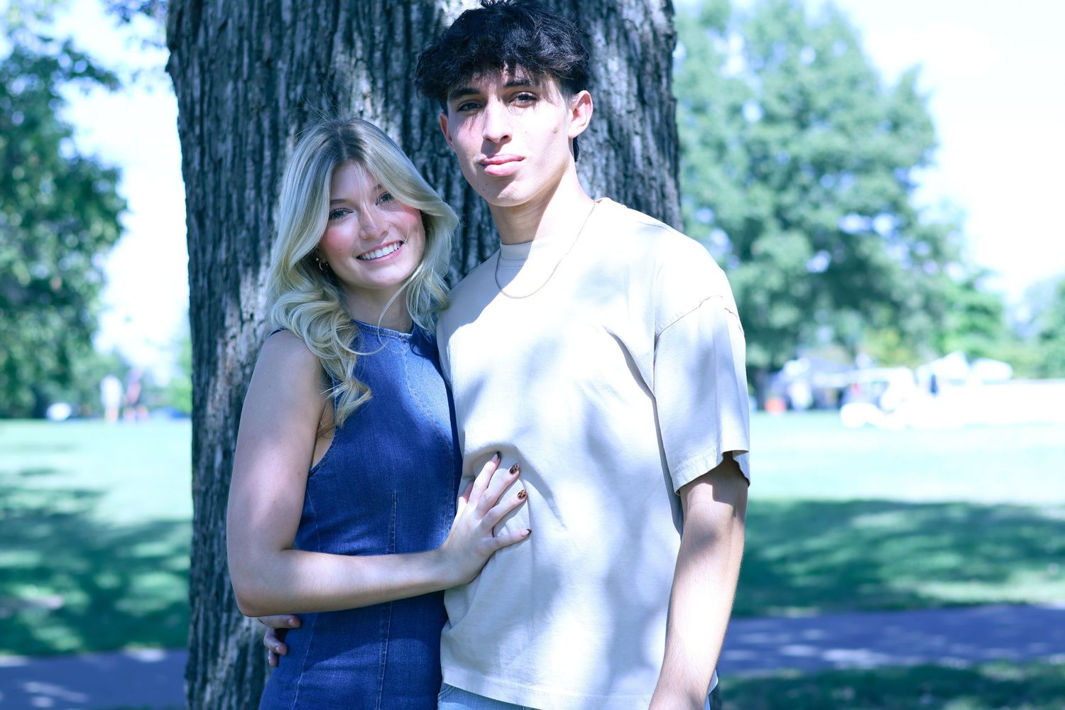 Playful couple photos taken near large tree trunk in park setting.
