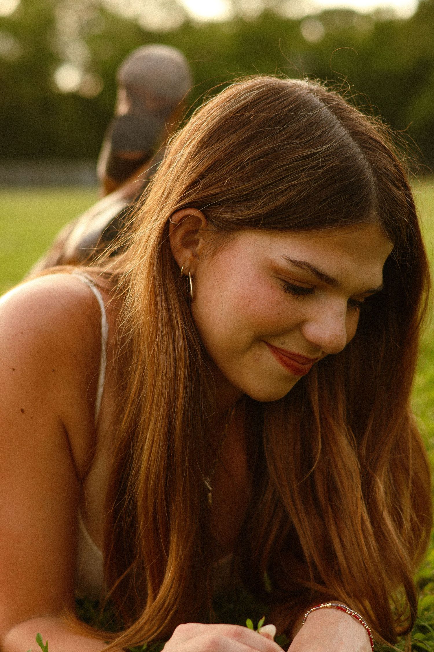 Young woman with long brown hair lying on grass smiling softly in warm golden sunset light.