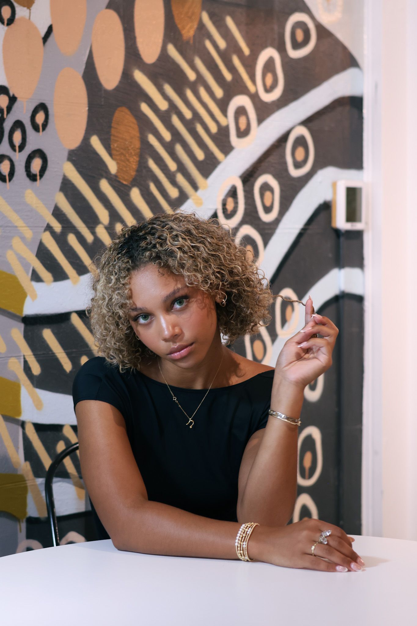 Stylish model in black top poses against artistic wall mural with geometric patterns.