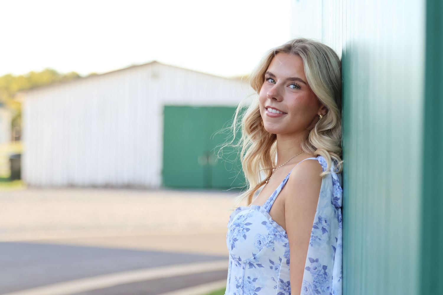 Someone in a blue floral dress poses against a mint green wall in natural lighting.