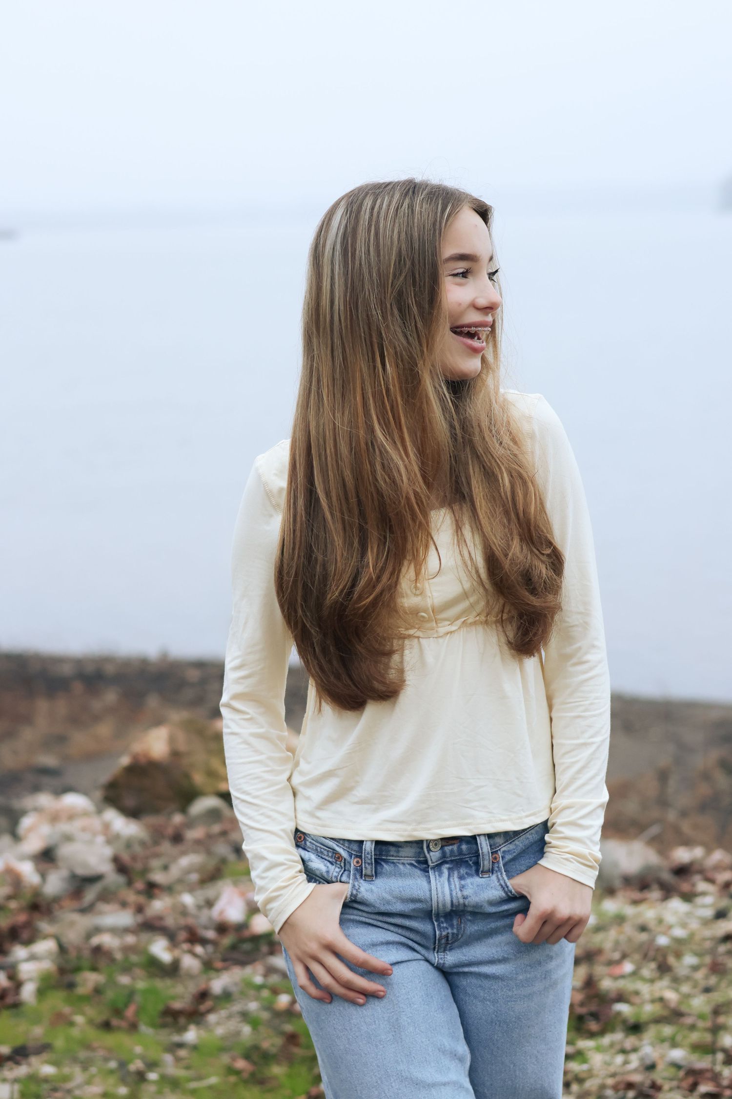 Person in cream sweater and jeans poses against rocky outdoor background in casual photoshoot series.