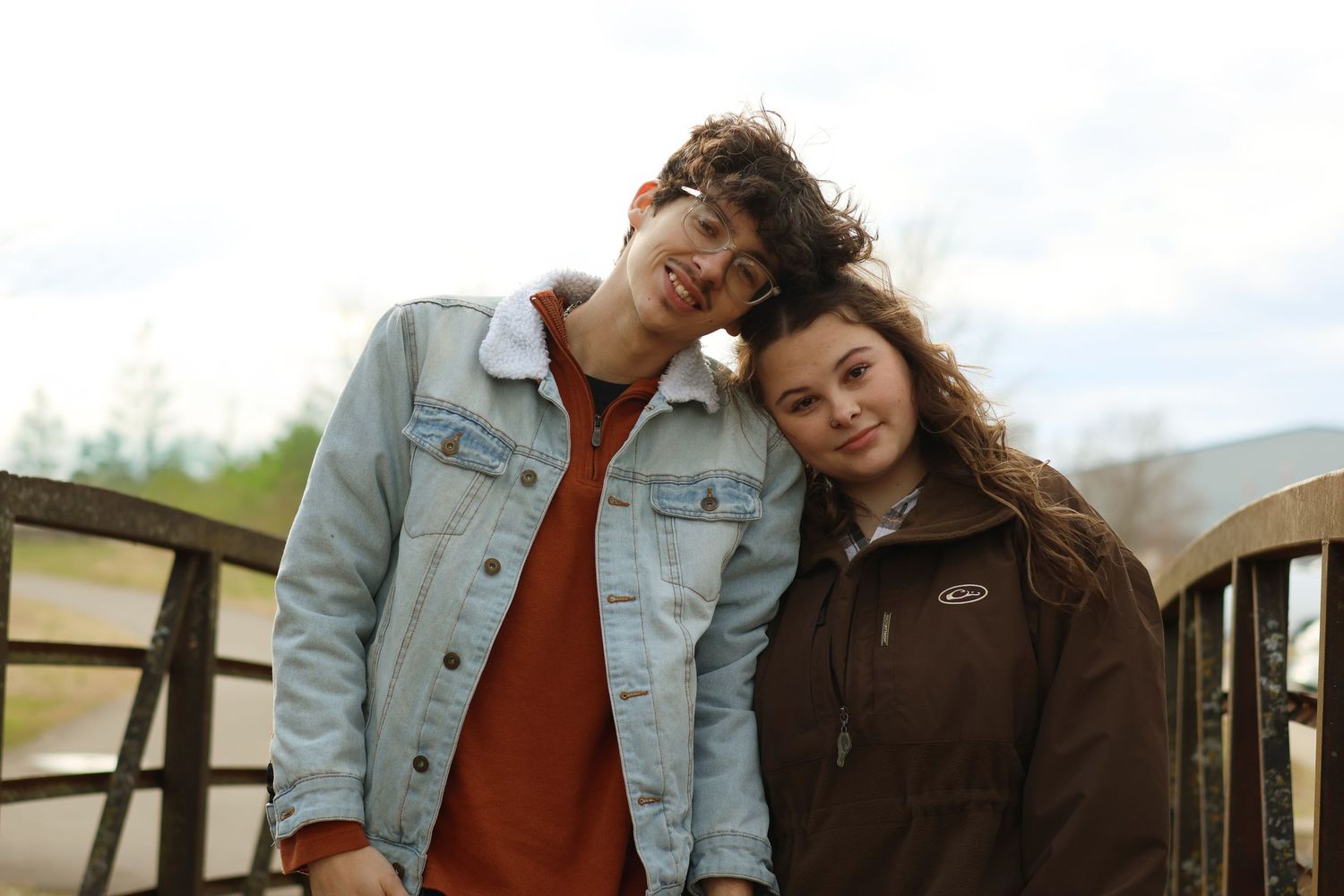 A group poses outdoors in casual denim and earth-toned clothing against a natural landscape backdrop.