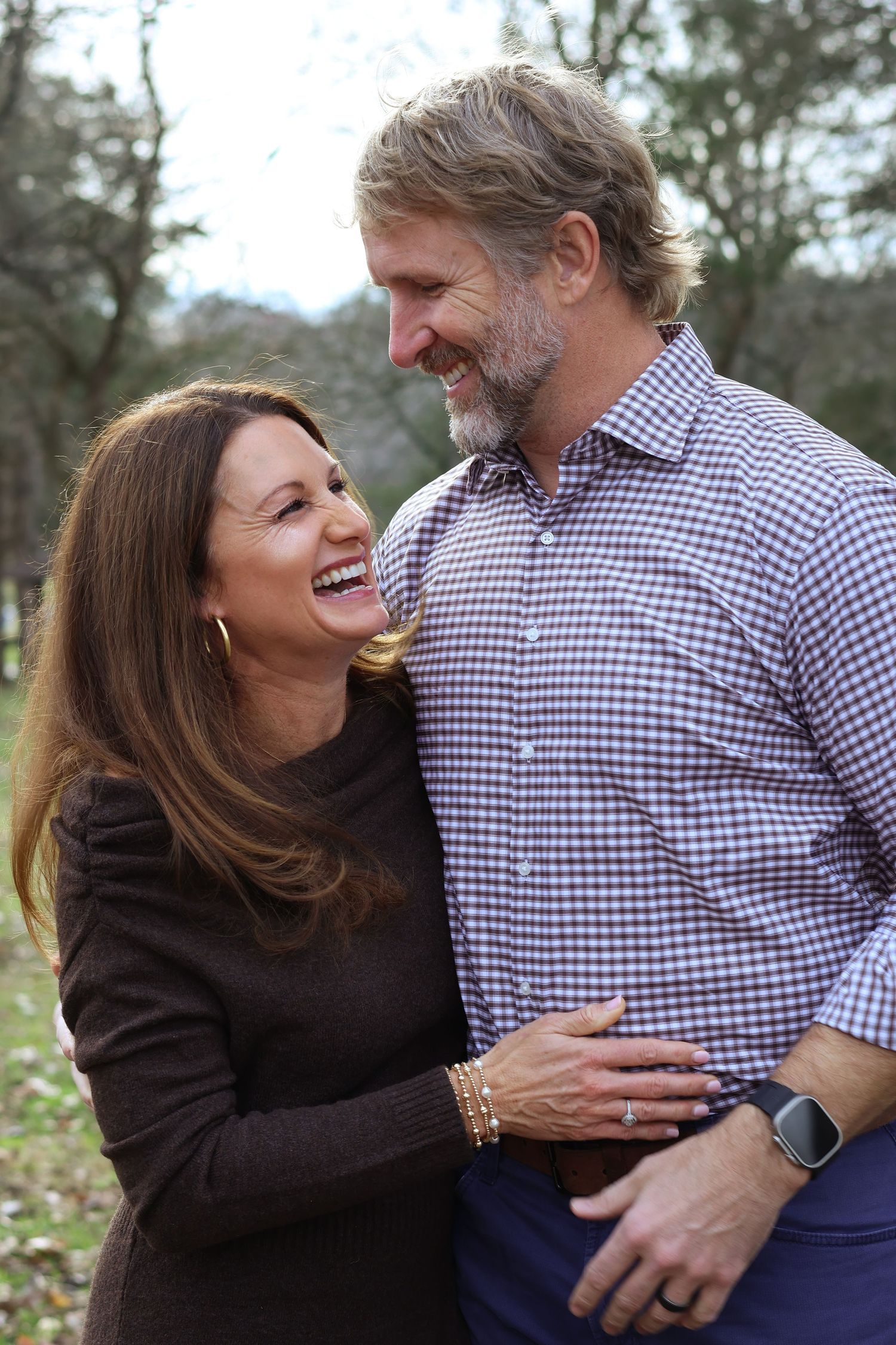 A happy couple shares a candid laughing moment outdoors while wearing casual fall attire.