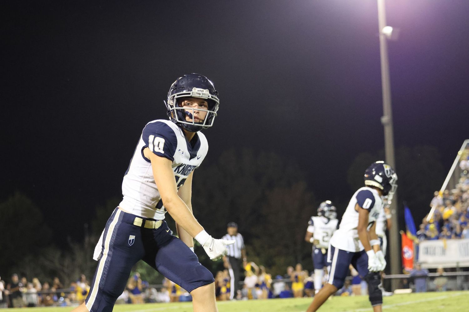Football players compete during a night game under bright stadium lights.