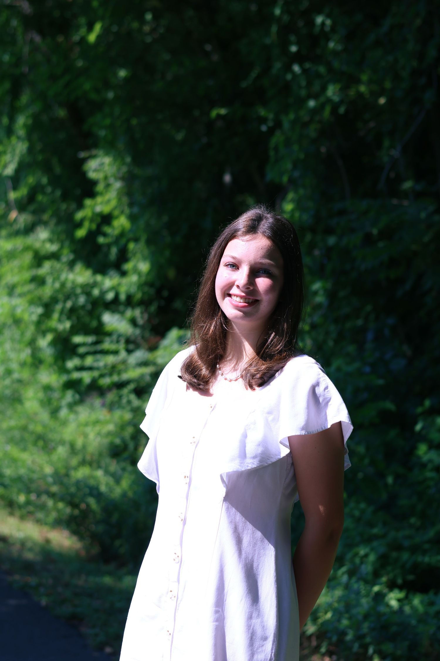 Person in white dress enjoying a sunny day in a green forest setting.