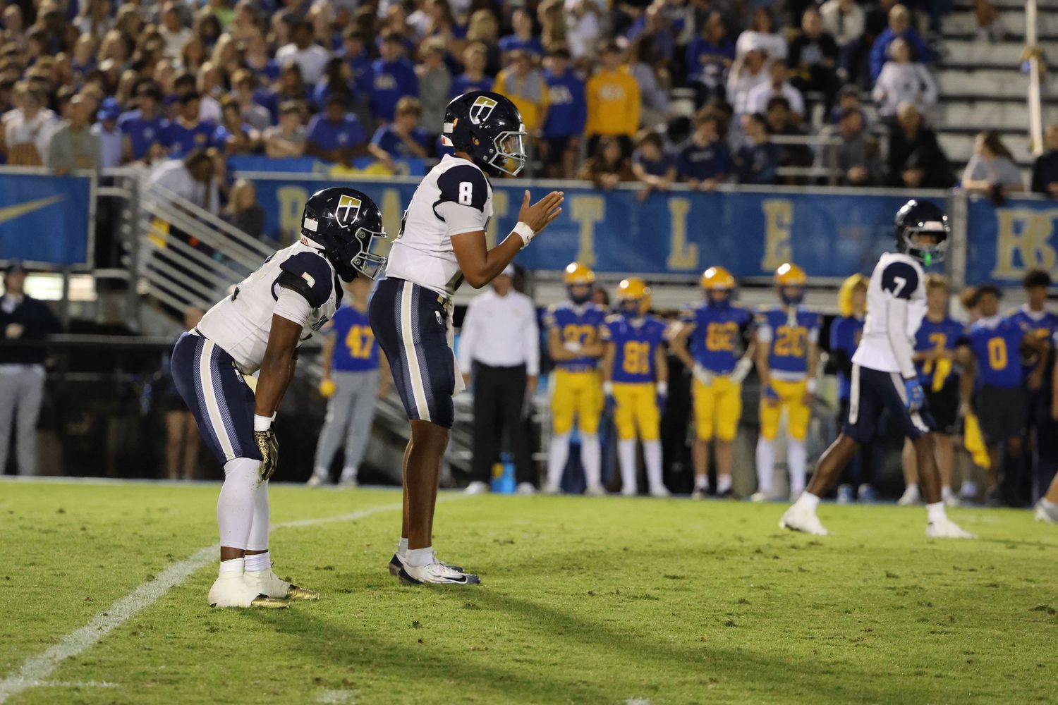 Football players in action on the field with crowded stadium bleachers in the background.