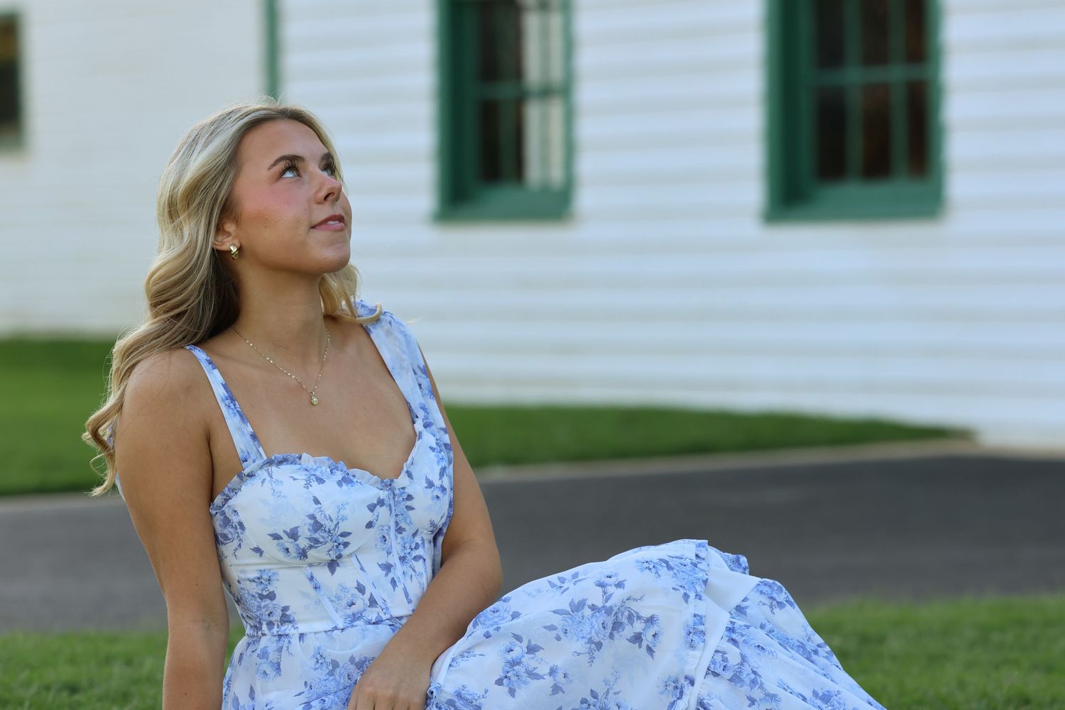 A person in a blue and white floral dress poses outdoors in front of a white building on a sunny day.