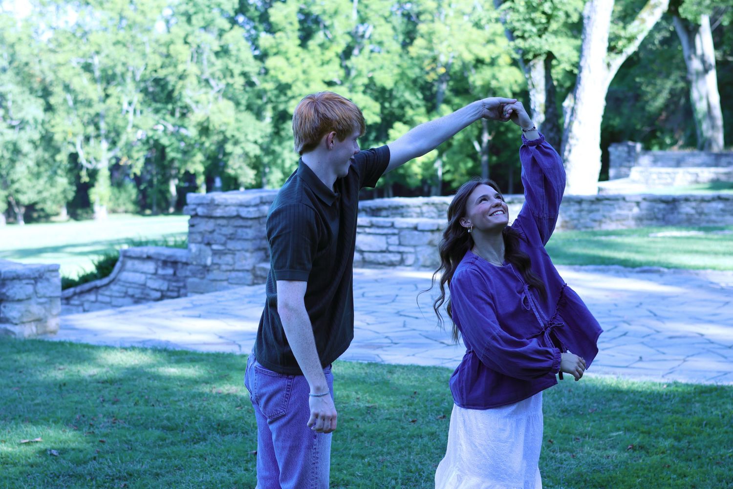 Playful couple dancing and twirling in a garden setting.