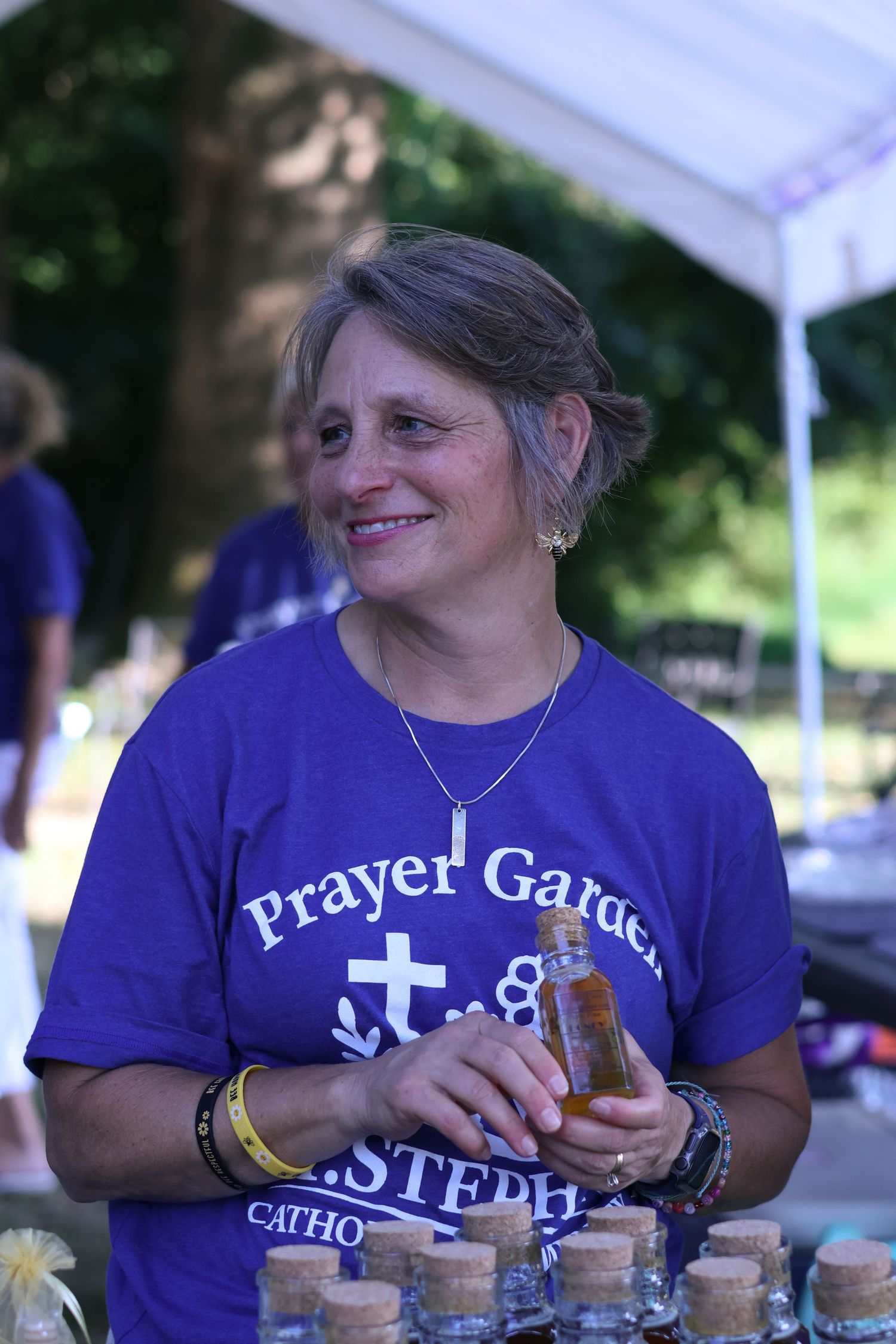 Person in purple Prayer Gate t-shirt smiling while working at an outdoor event booth.