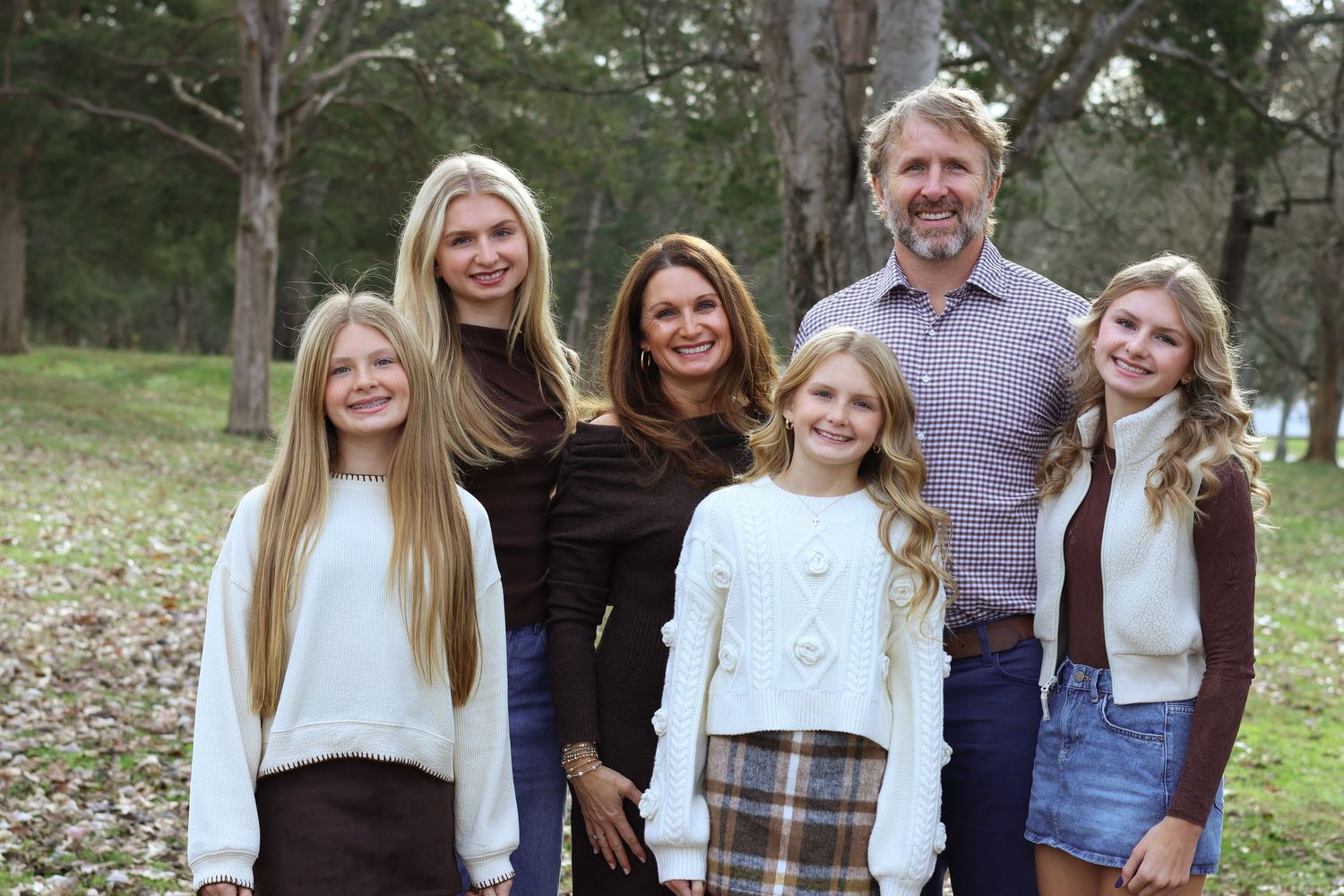 A group of five people standing together outdoors in casual clothing with trees in the background.