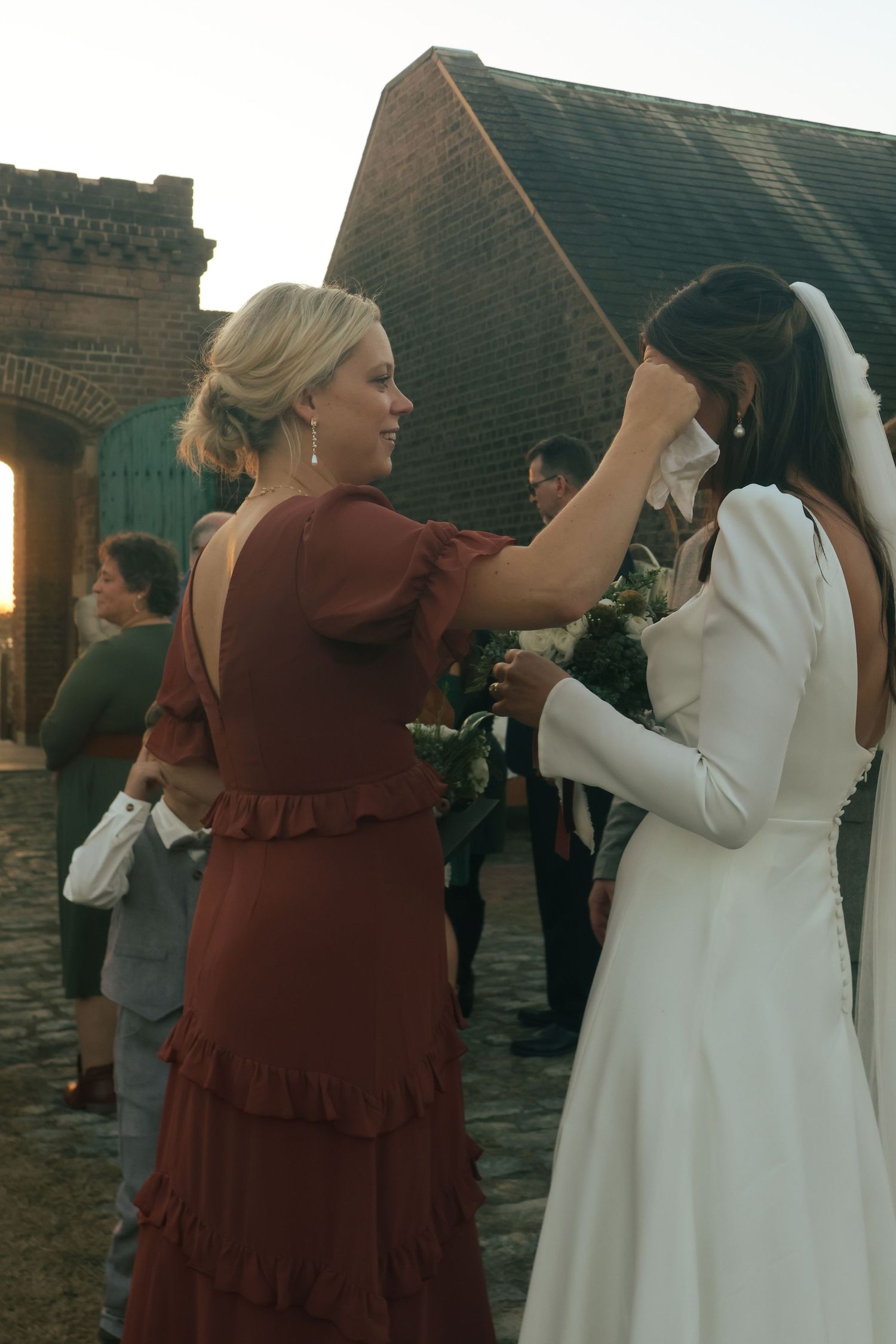 Two women in contrasting burgundy and white dresses dance together on a rooftop at sunset.