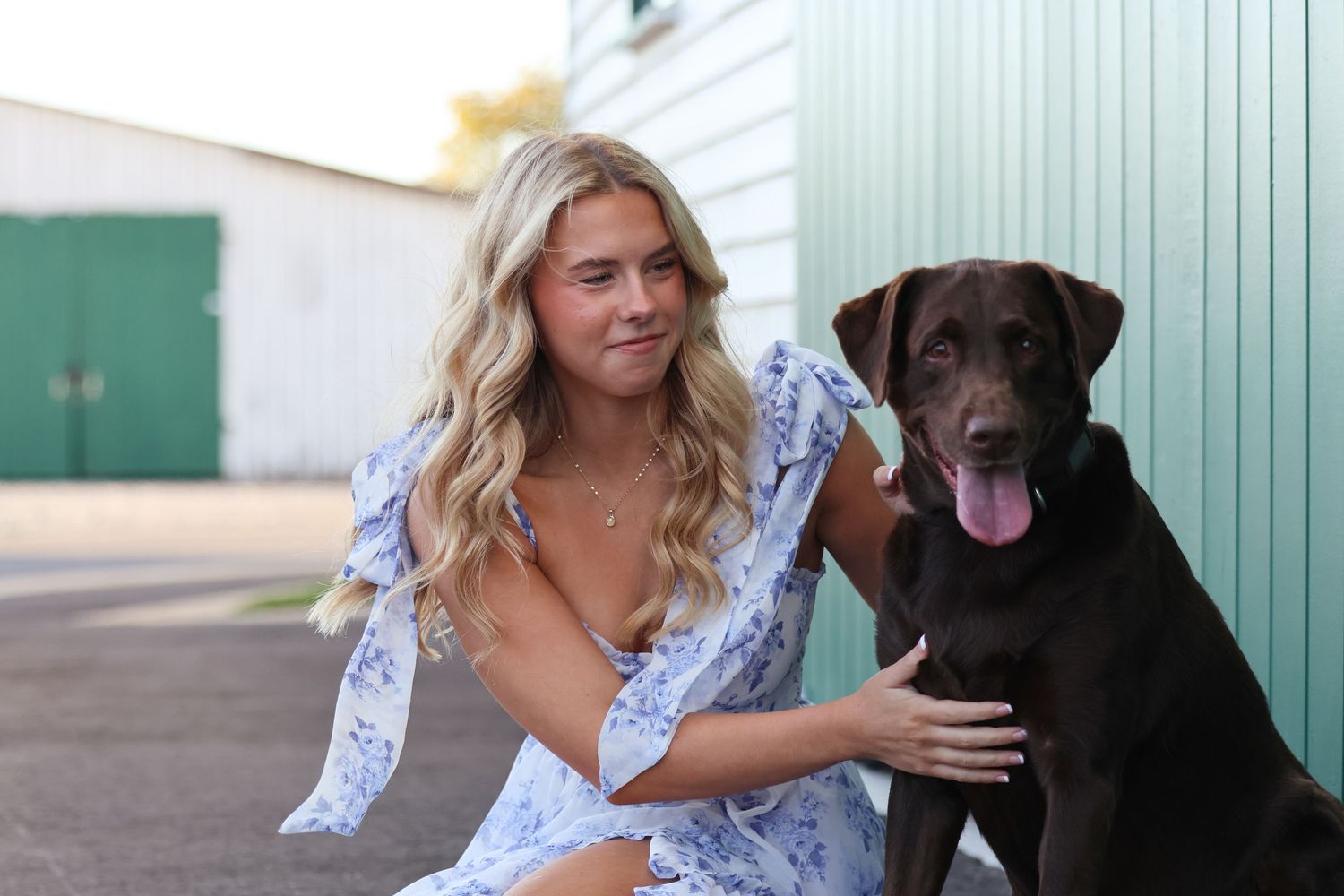 A chocolate Labrador and someone in a blue floral shirt pose against a mint green building exterior.