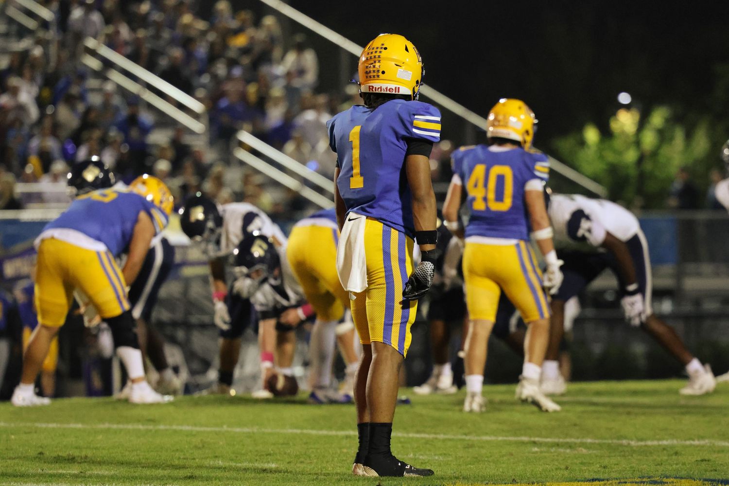 Football players in yellow and dark uniforms line up on the field during gameplay.