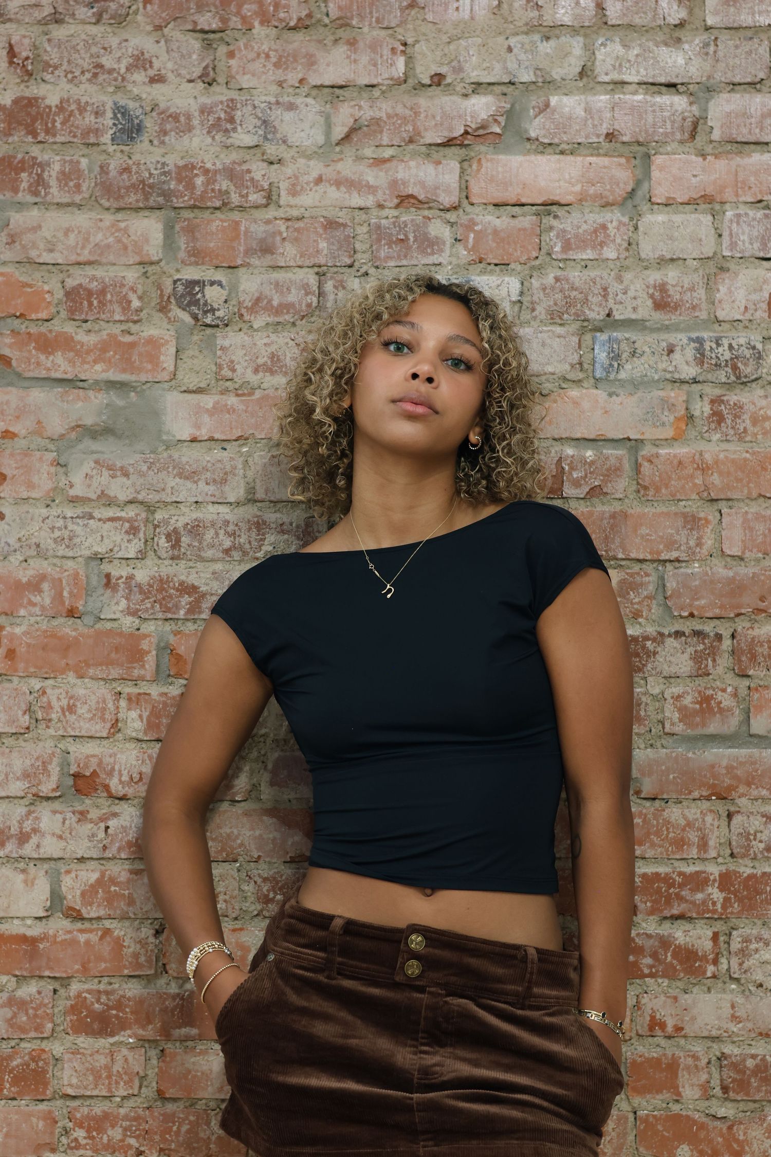 Fashion portrait against rustic brick wall wearing black crop top and brown pants.
