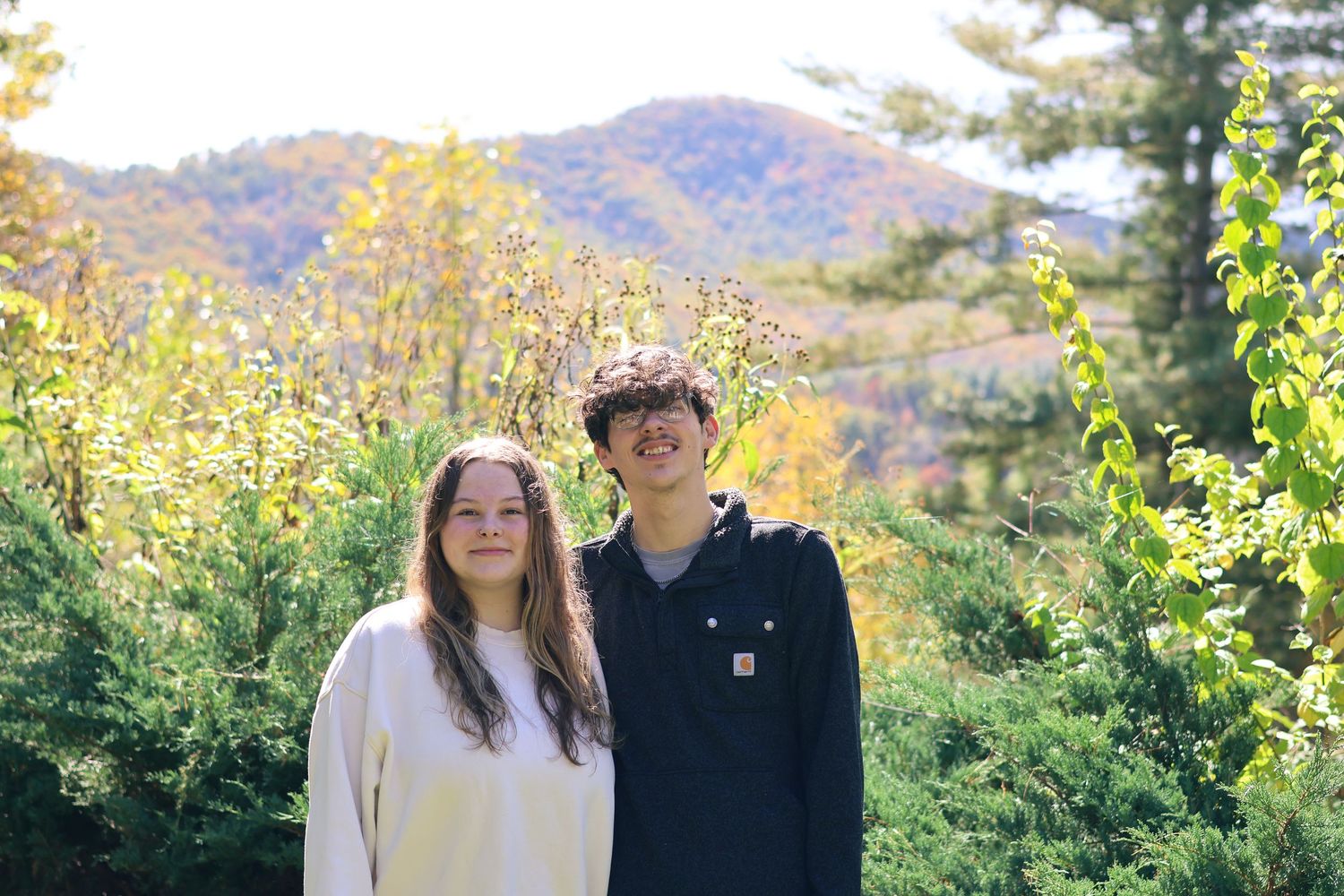 A couple in casual sweaters poses together with mountains visible in the background.