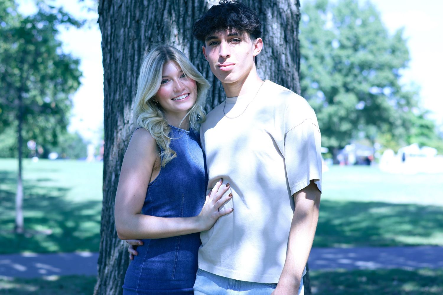 A couple in coordinating blue and white outfits poses by a tree in a park.